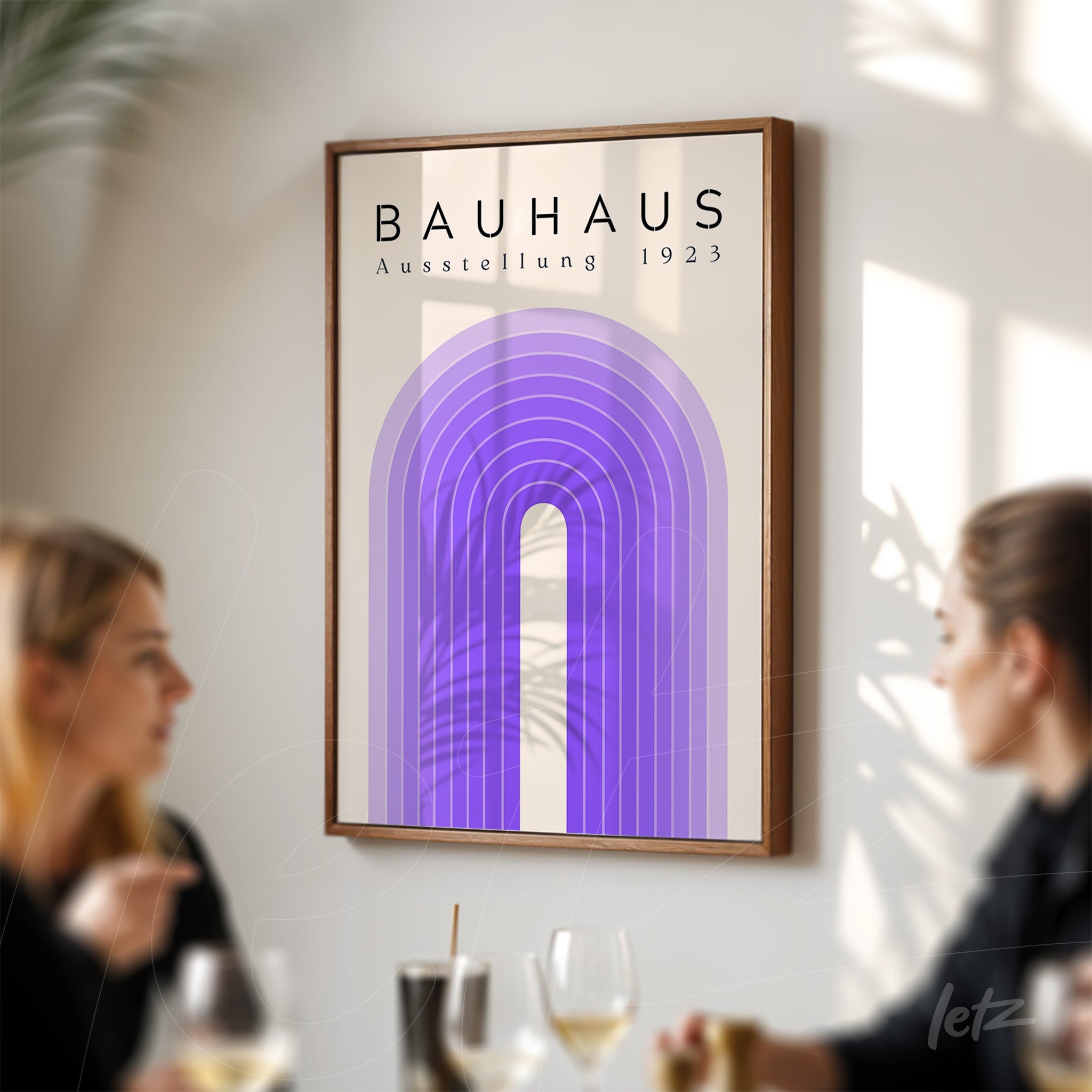 poster print with geometric purple design and text 'bauhaus ausstellung 1923', framed in wood and displayed on a wall next to a table with people
