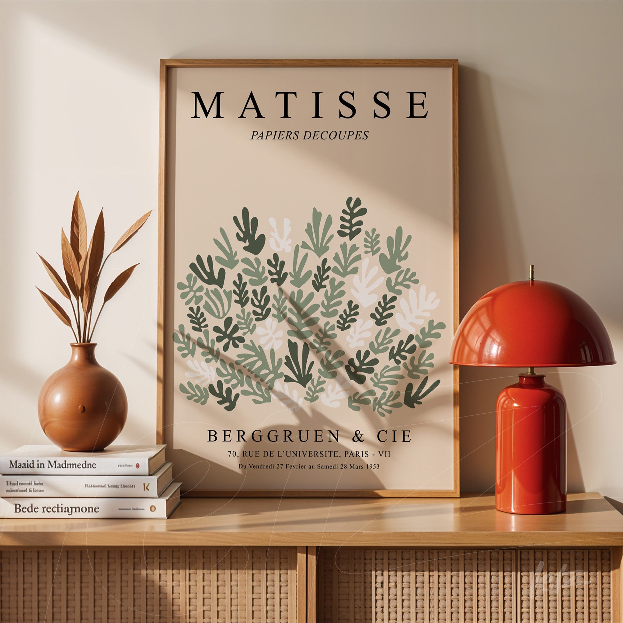 framed wall art featuring modern foliage design displayed on wooden table alongside red lamp and dried plant vase