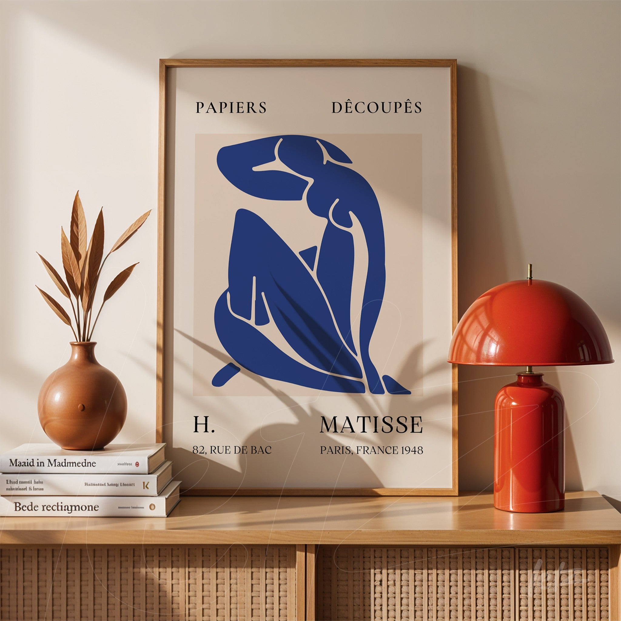 framed modern art print of a seated female figure in blue displayed on a wooden shelf