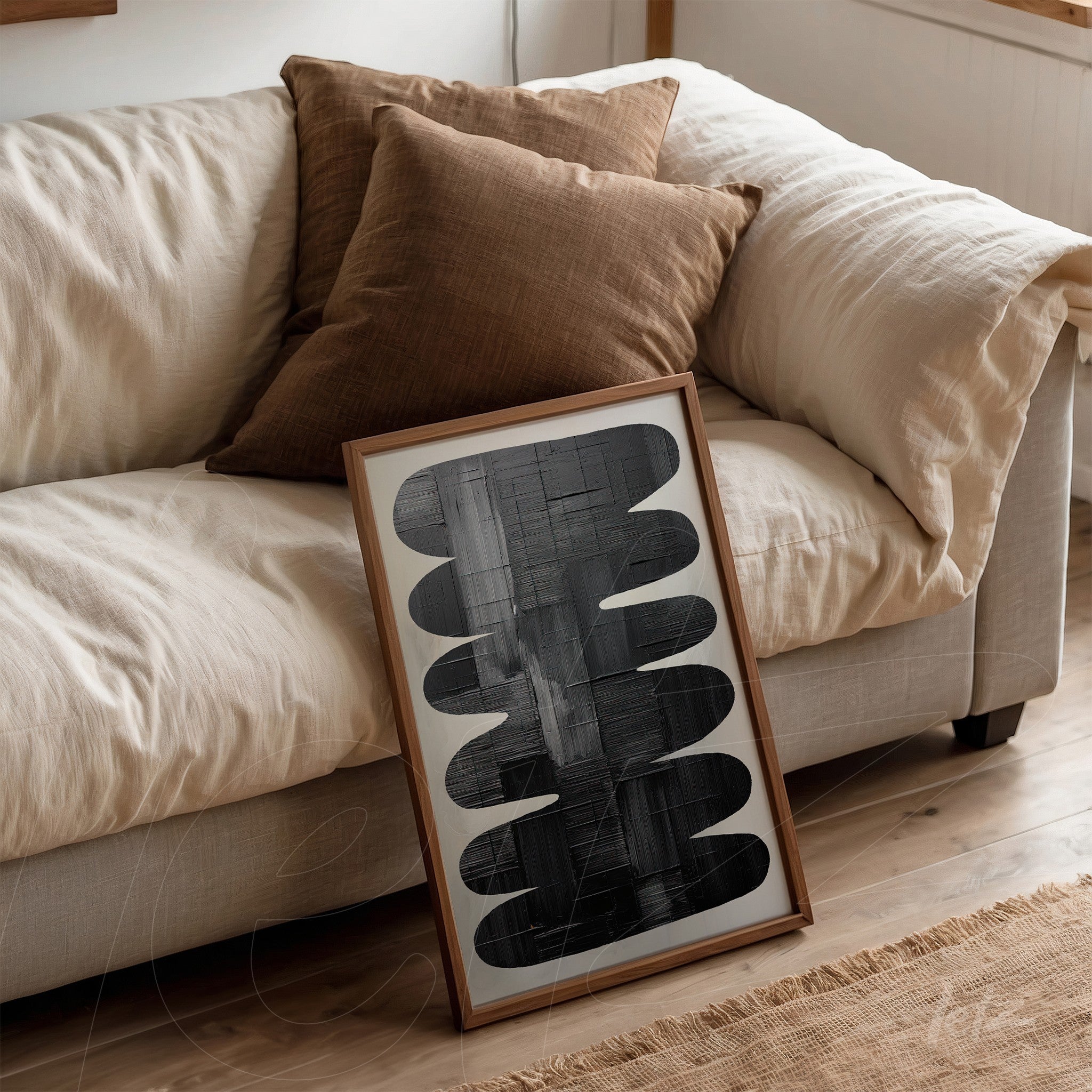 framed abstract art in shades of gray leaning against a light couch with brown cushions