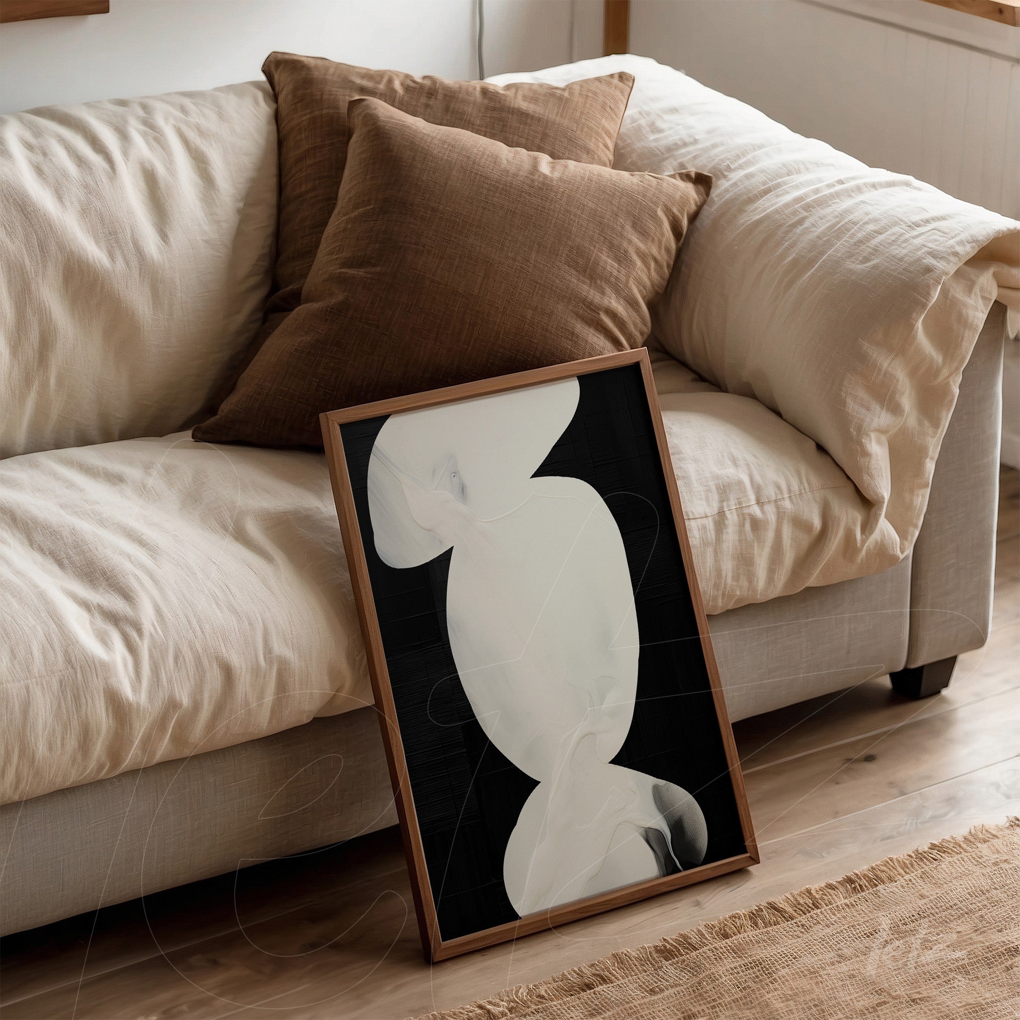 framed abstract art in black and white with light wooden frame propped against a sofa with brown cushions