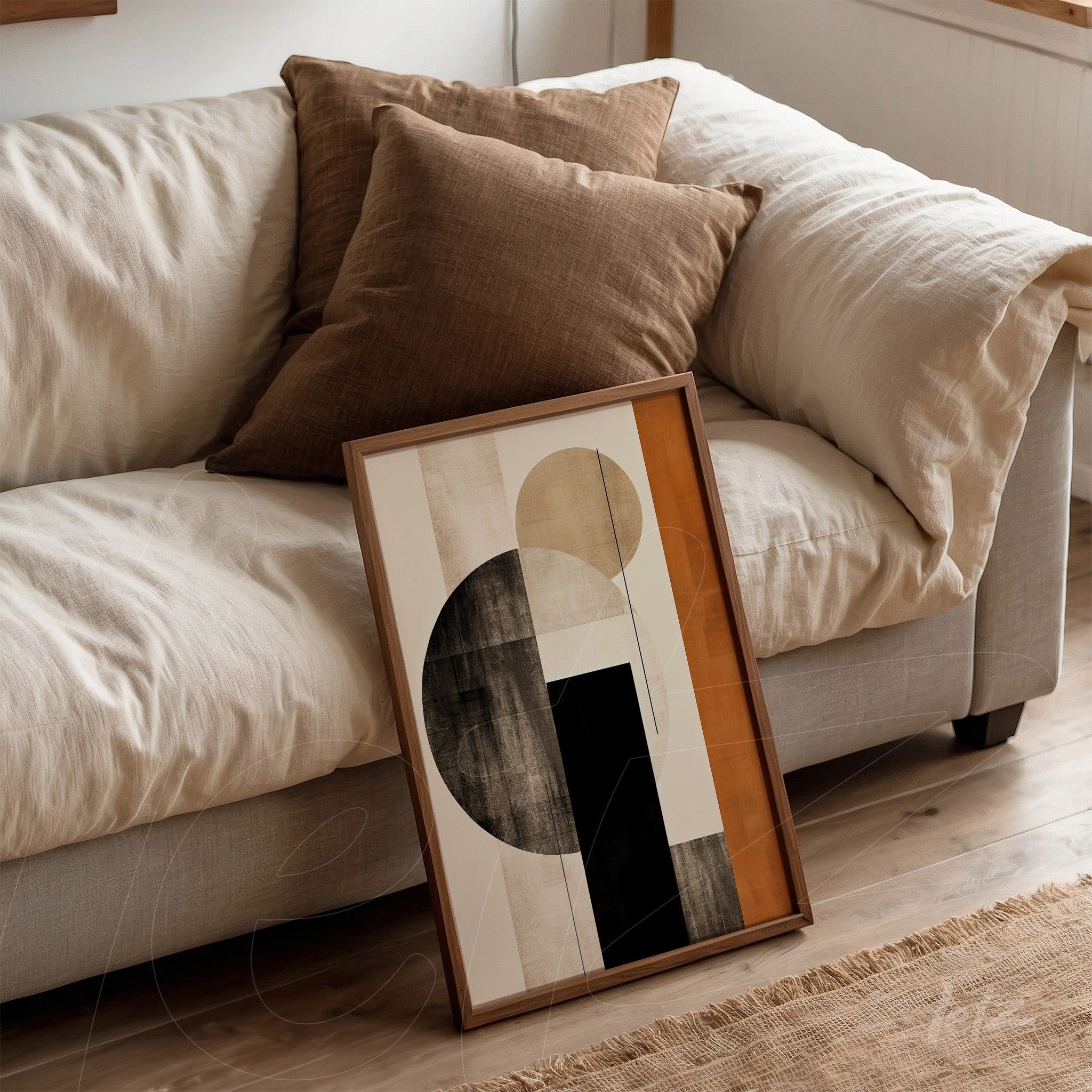 framed abstract wall art featuring a black circle with beige and orange details leaning against a brown sofa with decorative pillows