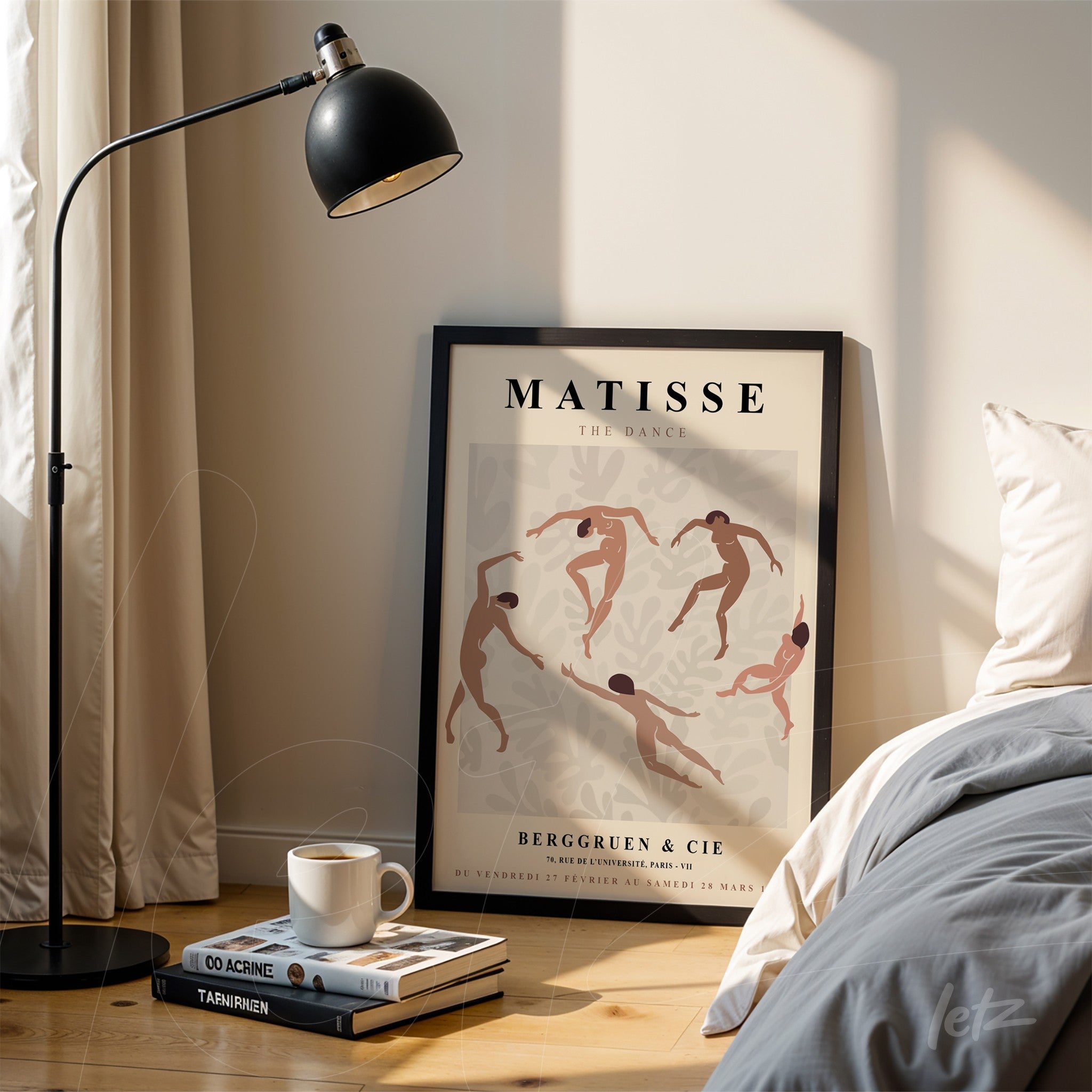 framed figurative artwork of dancers in a black frame, leaning against a bed with a gray blanket