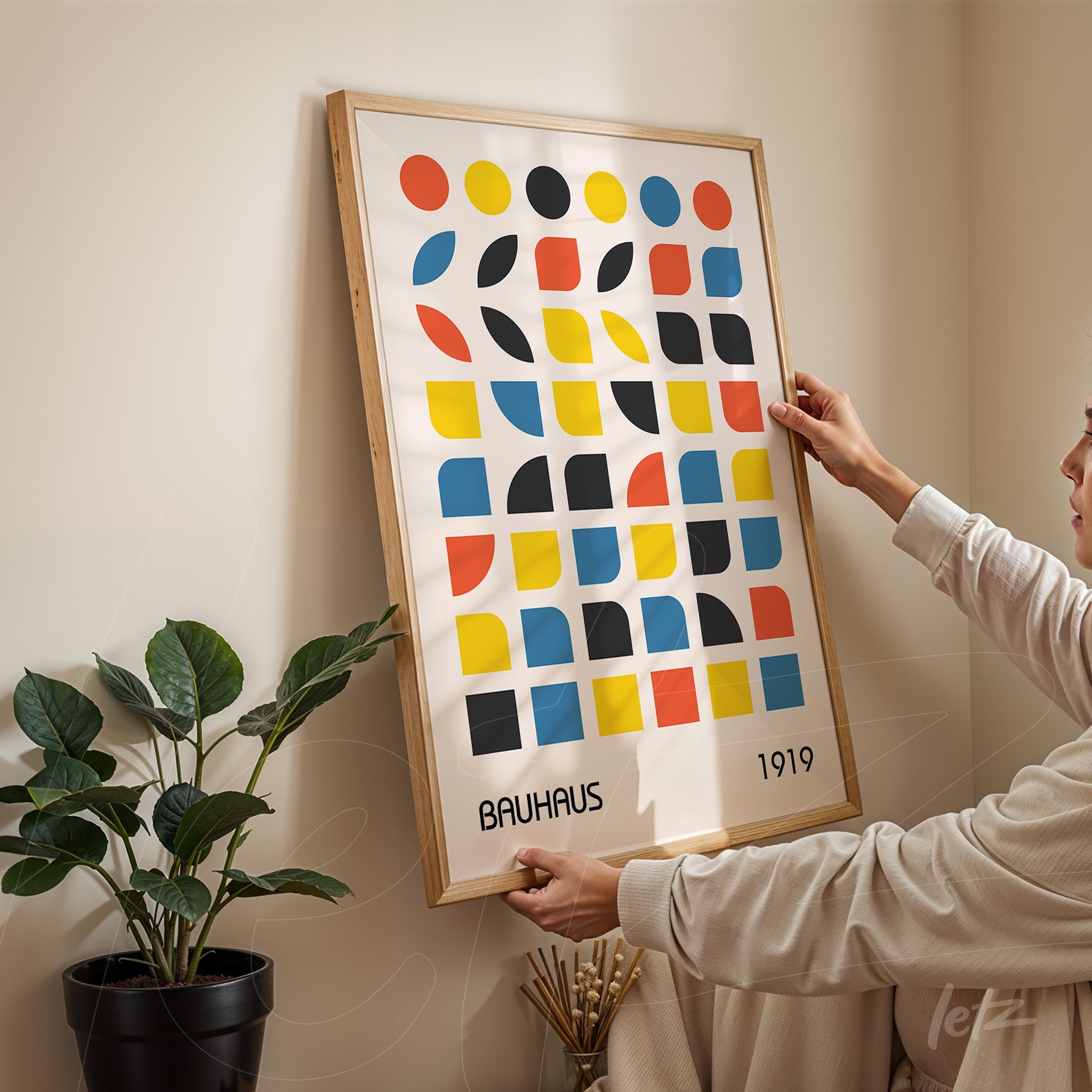 poster featuring colorful geometric bauhaus style art in light wood frame being placed against beige wall