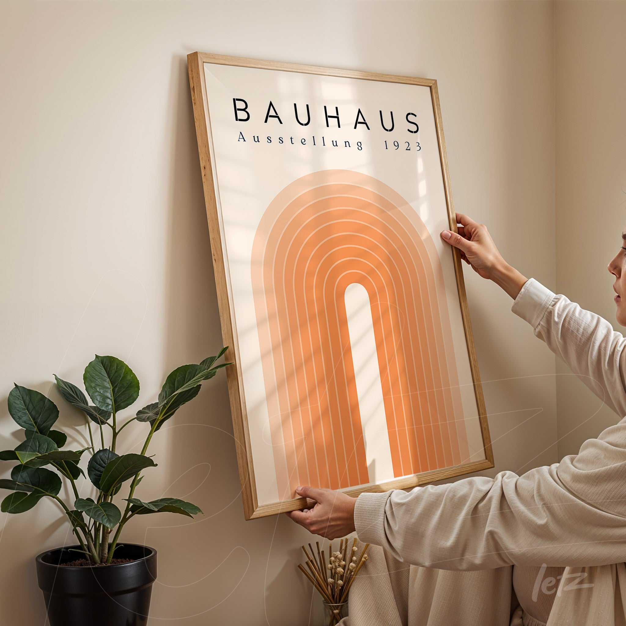 retro style poster of concentric orange arches in a light wood frame, displayed on a beige wall next to a potted plant