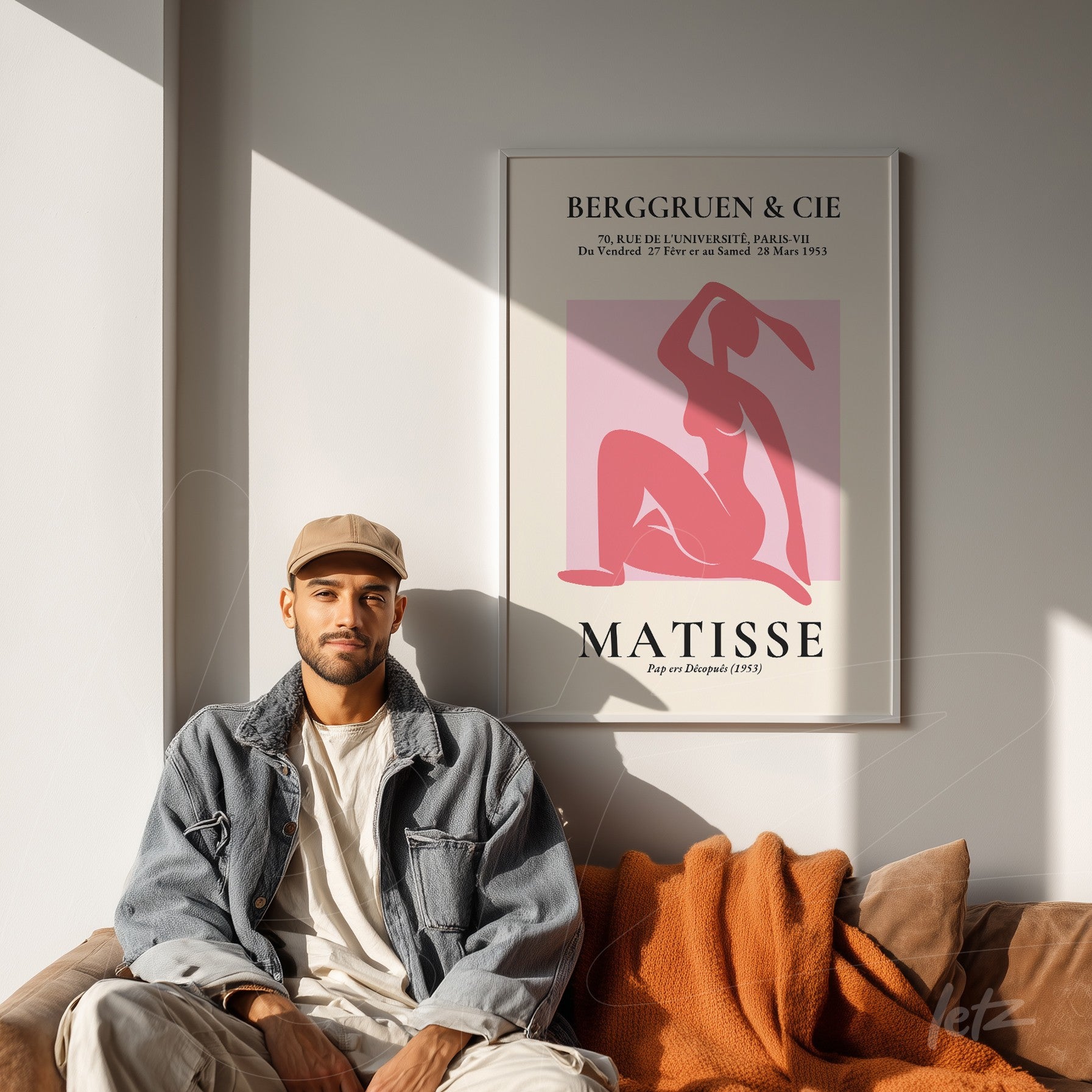 framed art print of Matisse on a white wall accompanied by a man sitting beside it wearing a denim jacket and cap