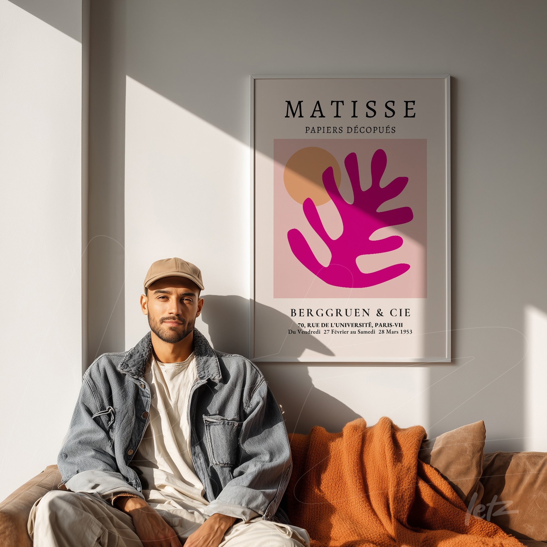 framed artwork of Matisse in shades of pink and orange displayed on a light wall with a man sitting on a couch wrapped in an orange blanket