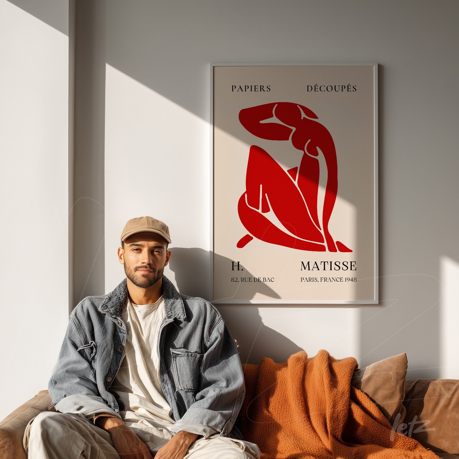 framed modern art of a red female figure against a light background displayed on a light wall next to a sofa with an orange blanket