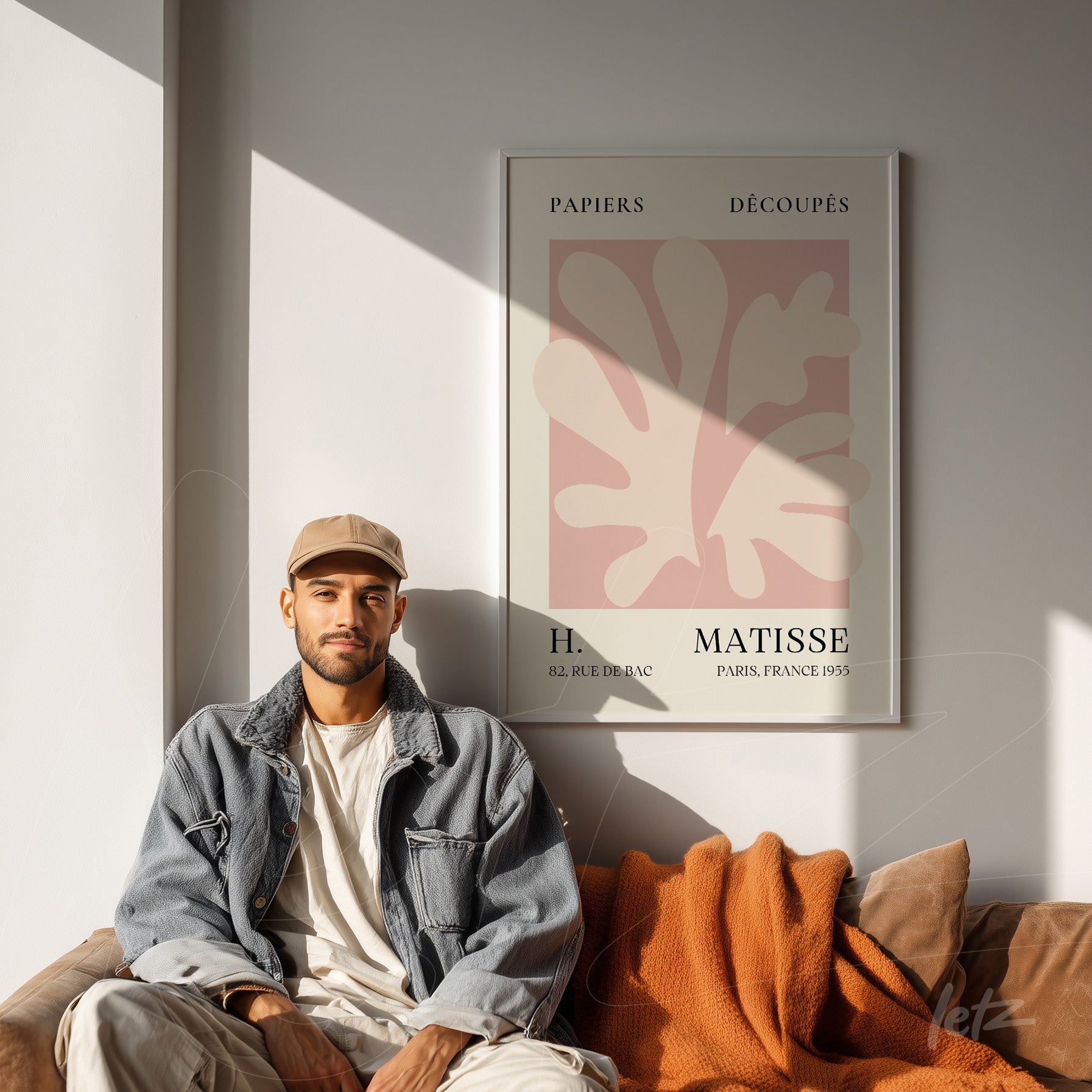 decorative wall art featuring henri matisse design in white frame displayed on light wall with brown sofa and orange blanket in the background