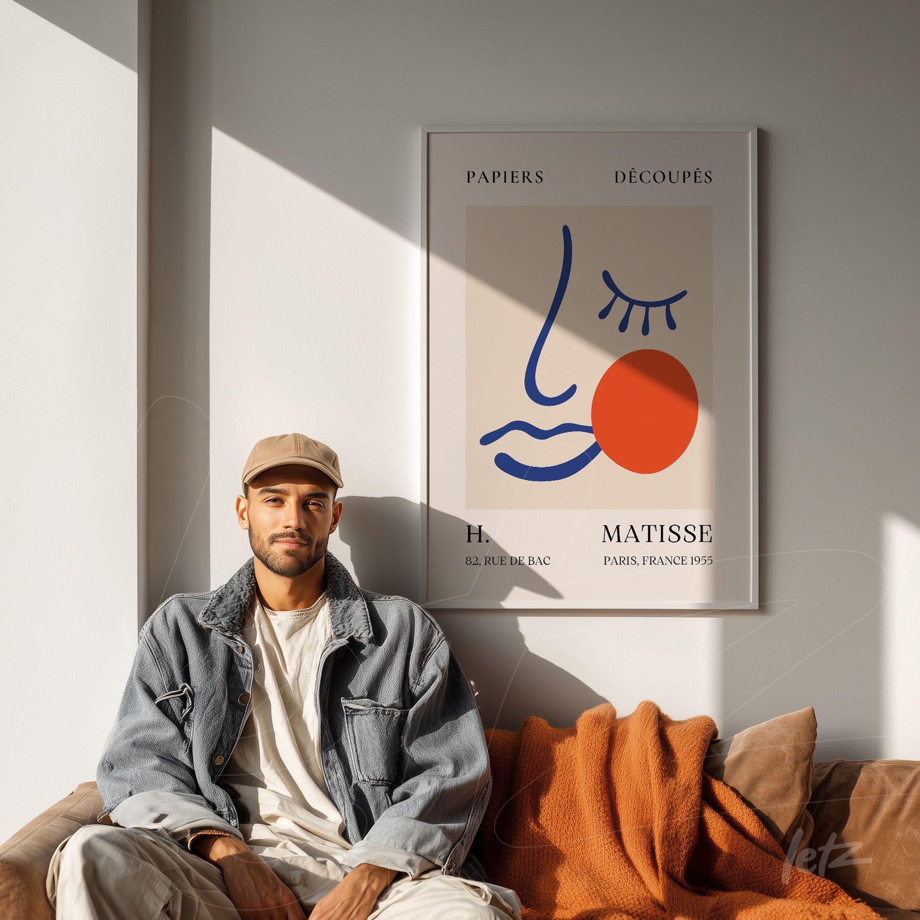 framed wall art featuring an abstract female face design in light frame with a man sitting on a sofa draped in an orange blanket