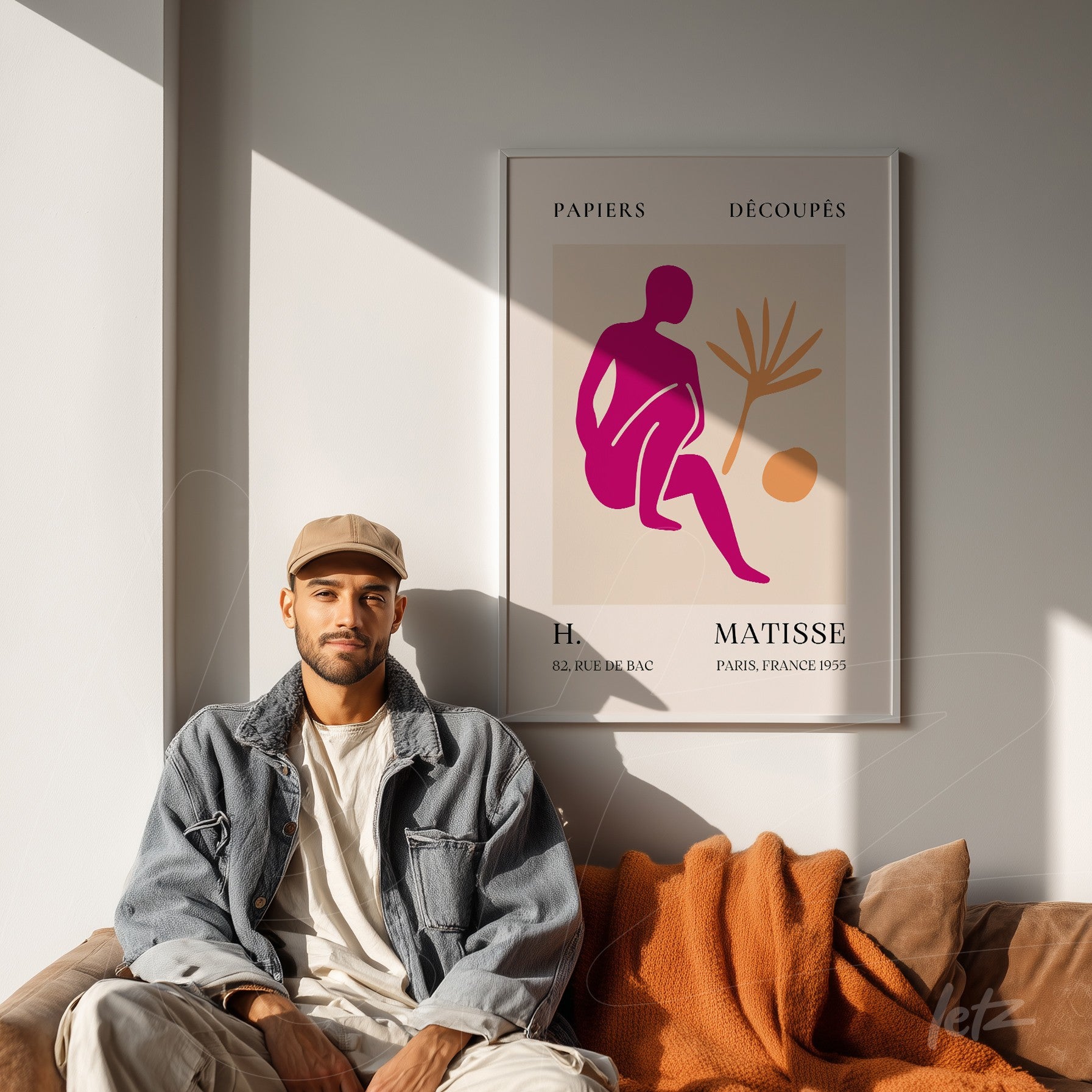 framed wall art featuring an abstract representation of a female figure in pink and orange tones displayed on a neutral wall beside a man sitting on a leather couch