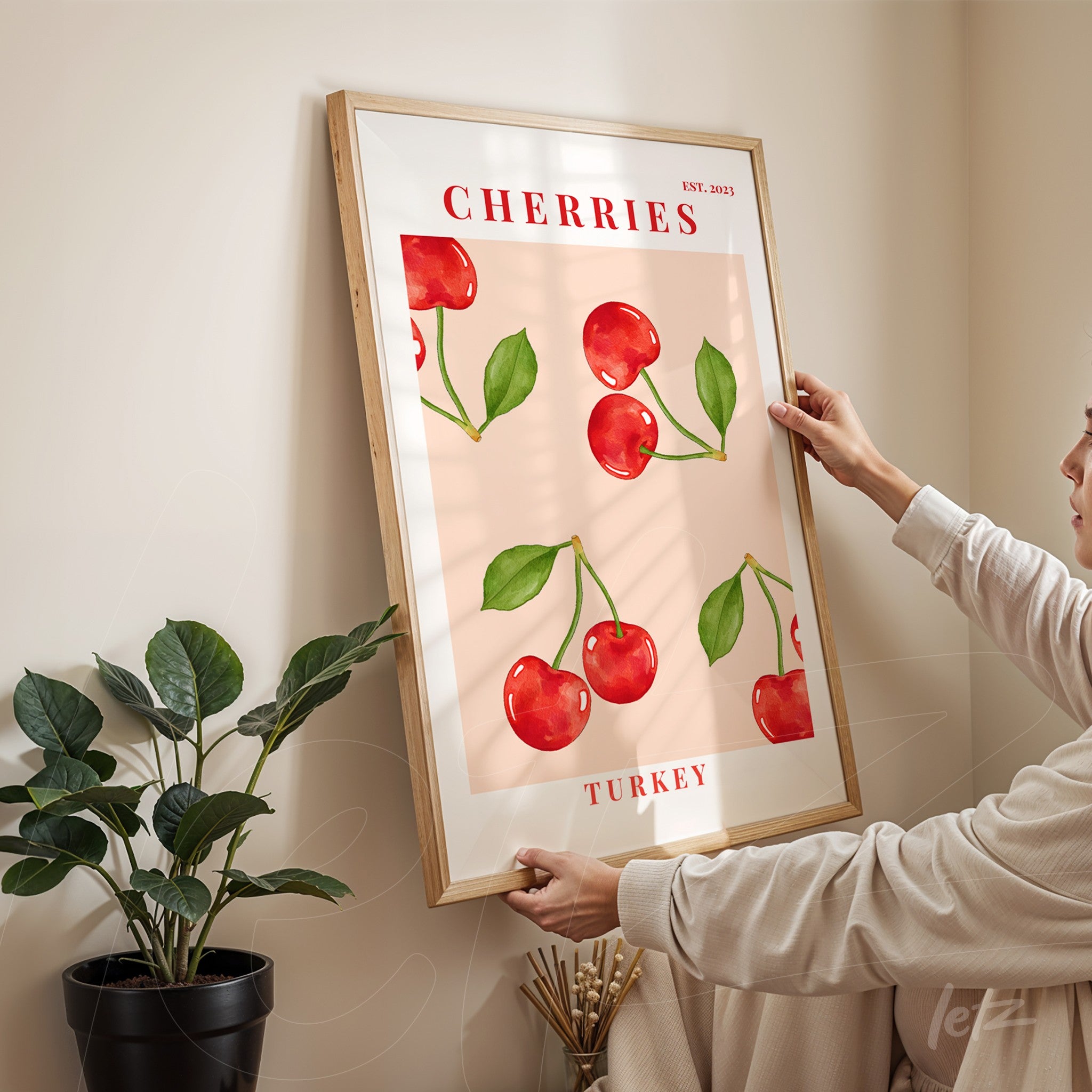 framed wall art featuring red cherries on pink background with light wood frame