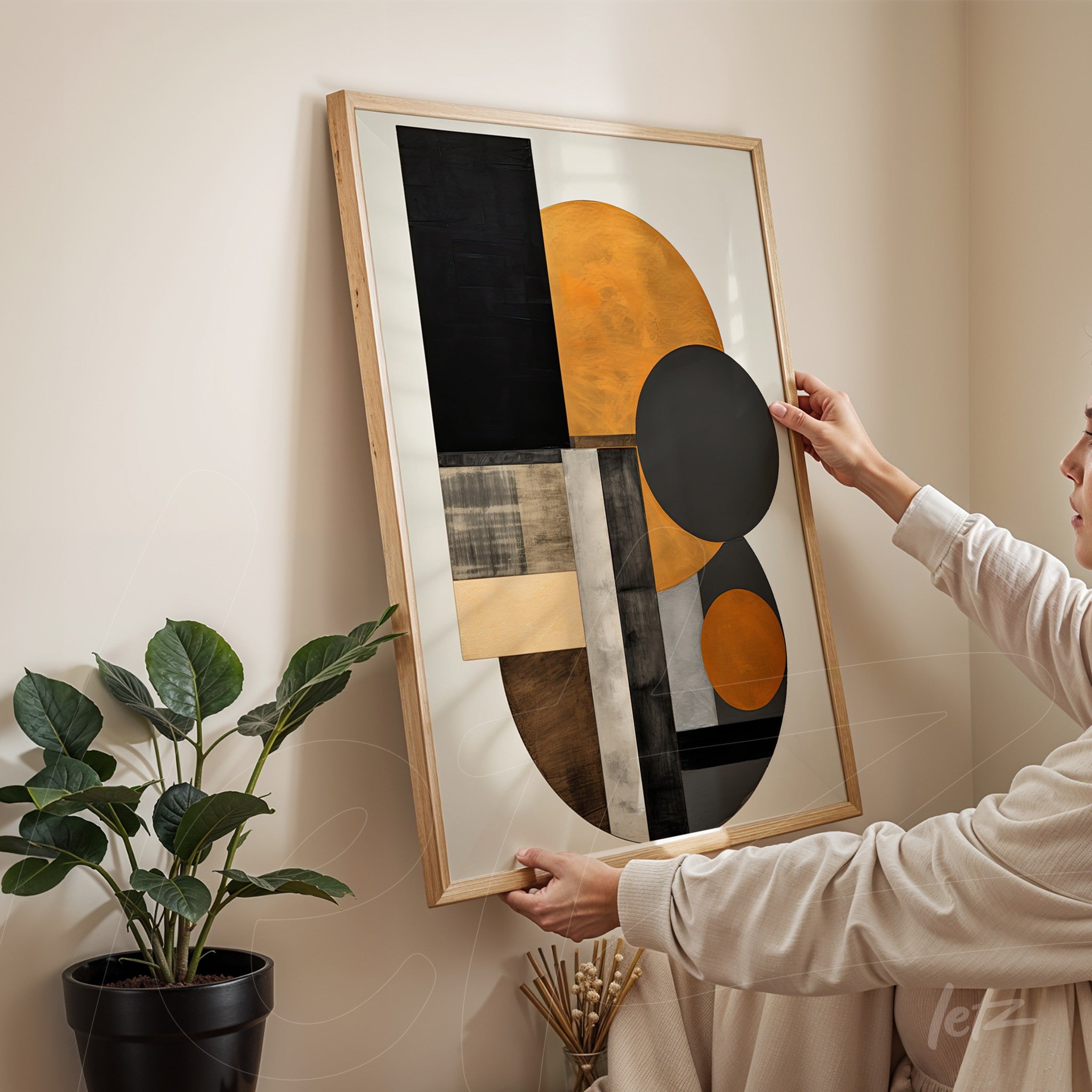 abstract artwork in orange and black, light wood frame, held by a person in a setting with a plant