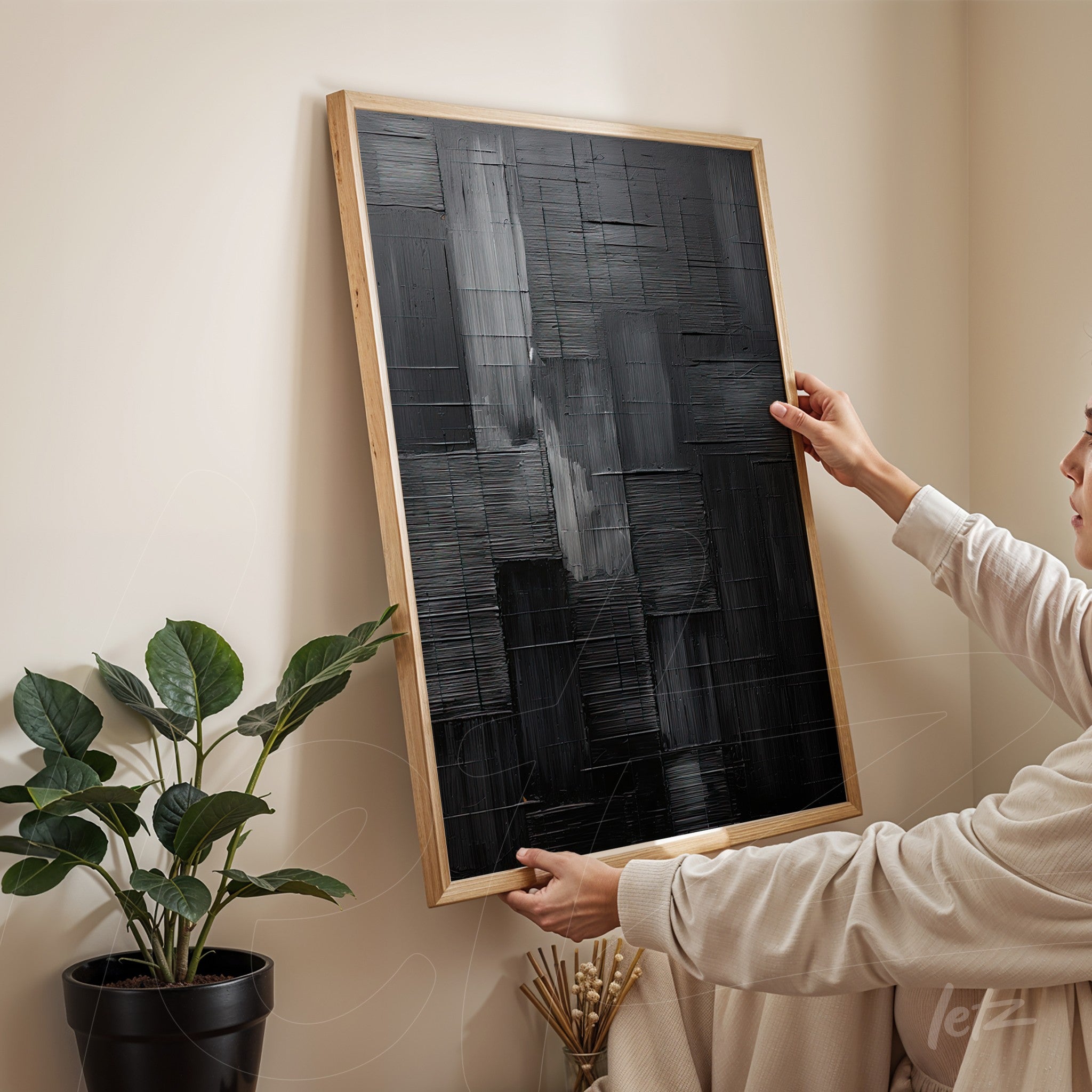 abstract wall art in black tones with a light wood frame being held by a person in a minimalist setting