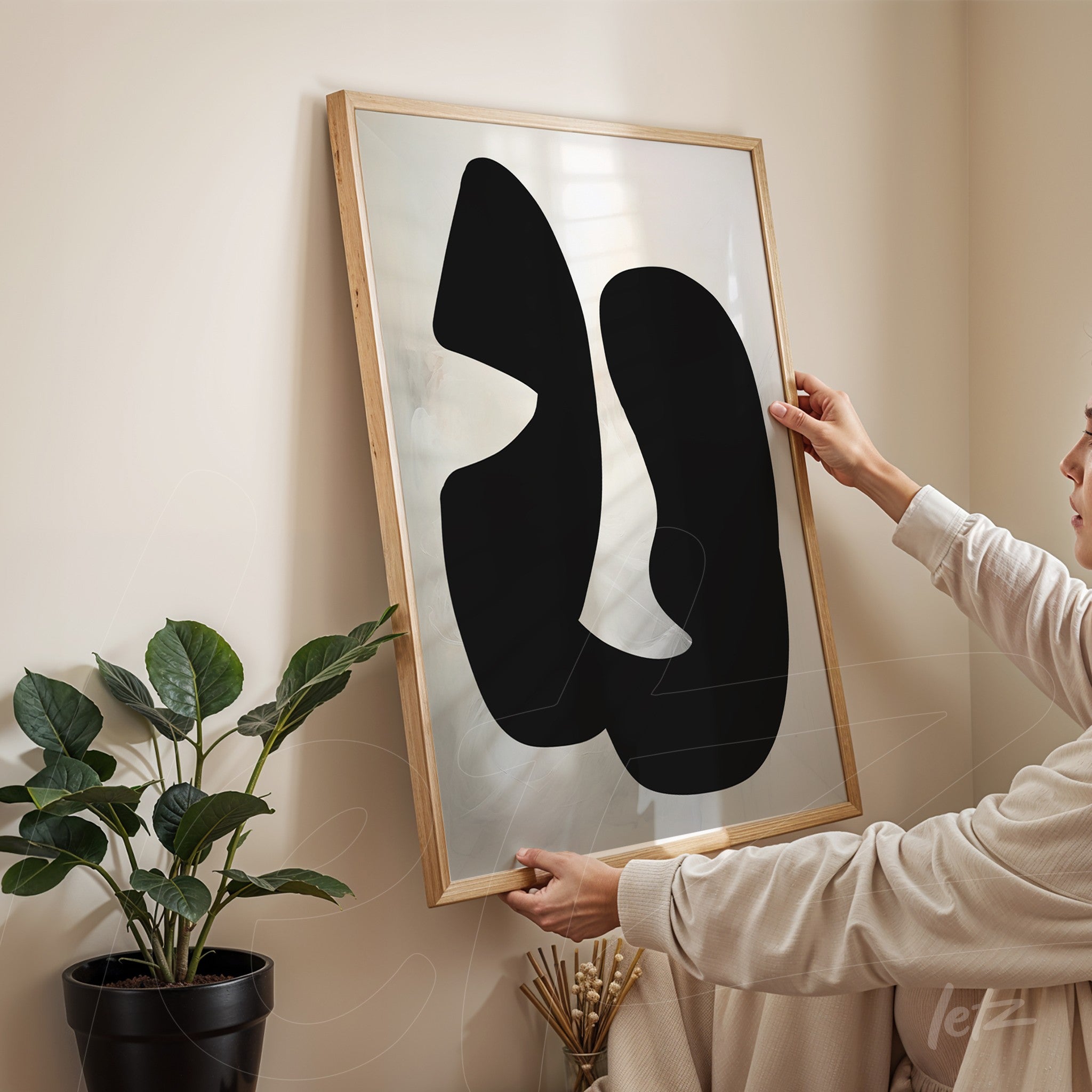 modern art piece featuring abstract black shapes, held by a person in a cozy setting with light wood frame