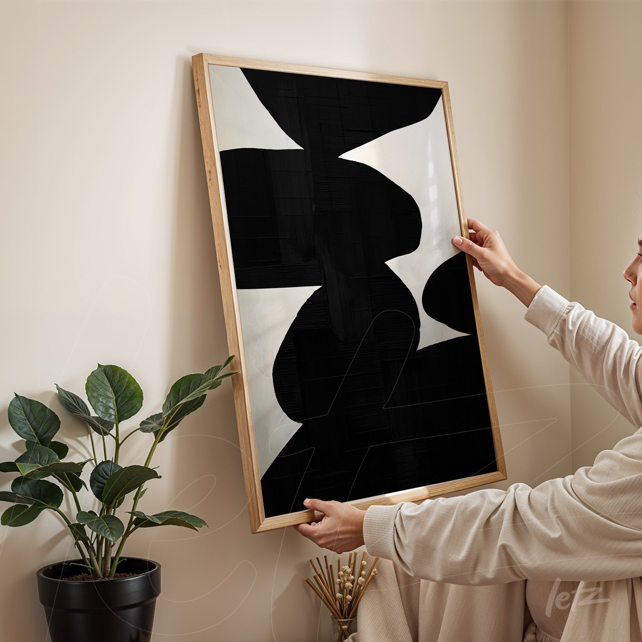 abstract art framed in light wood featuring black and white shapes held by a person in a cozy setting