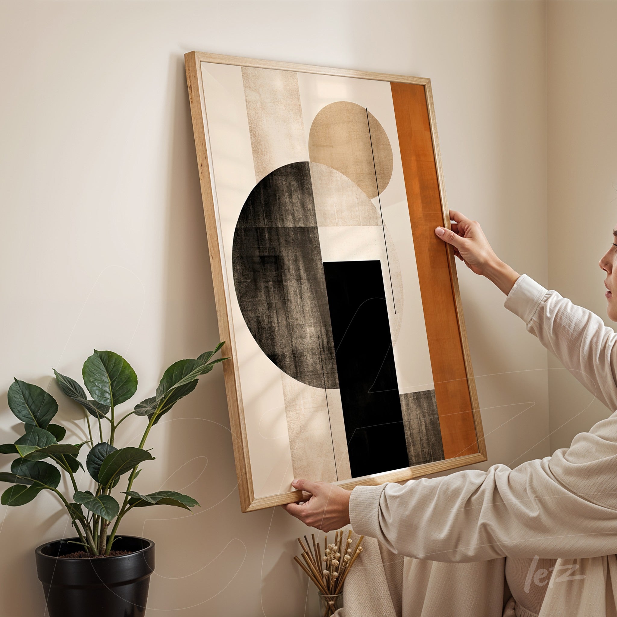 abstract wall art featuring geometric shapes in black, beige, and orange held by a person in an indoor setting with a plant in the background