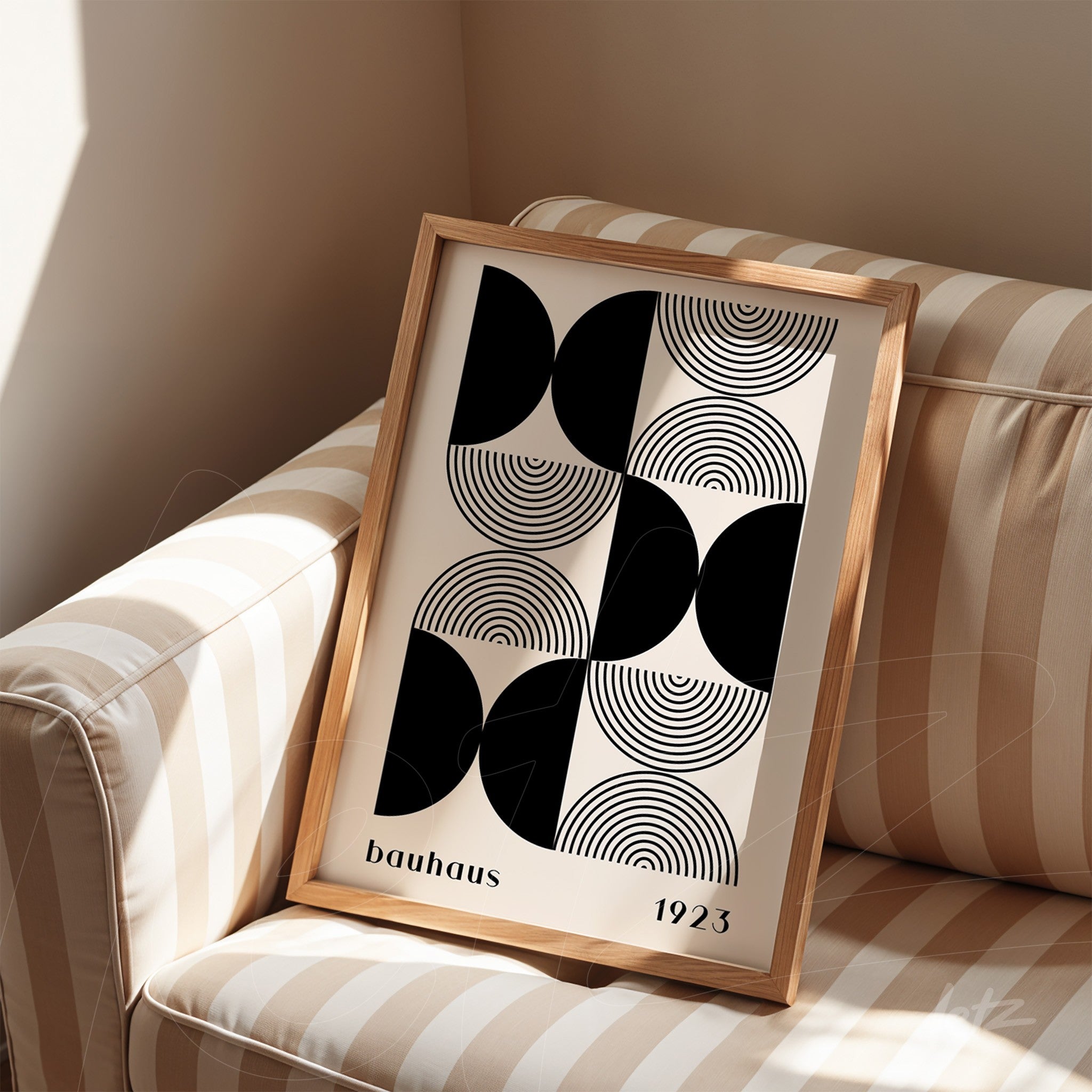 decorative framed print with black and white geometric art in light wood frame resting on striped sofa