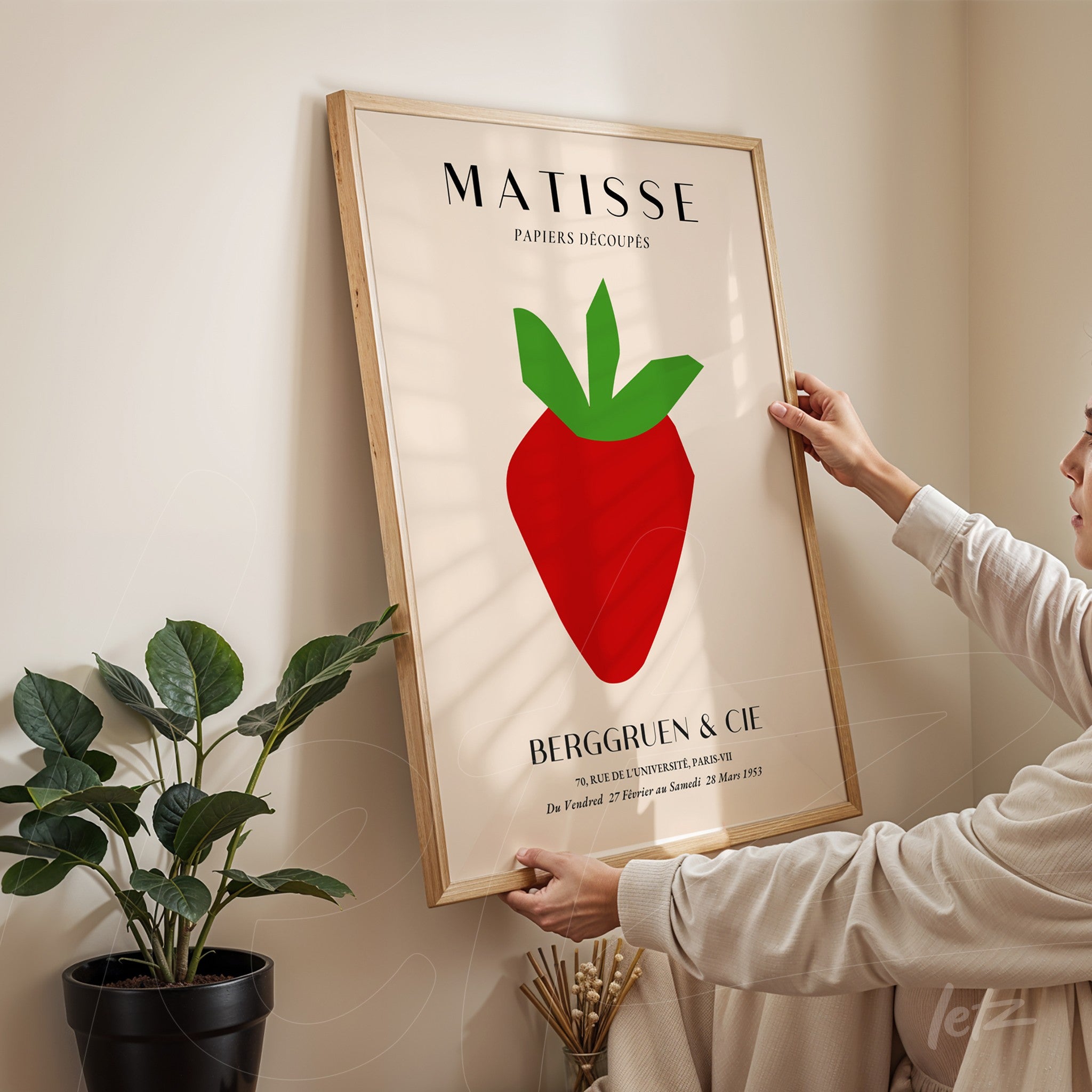 framed modern art print of a red apple on a light background, natural wood frame, person adjusting the artwork on the wall
