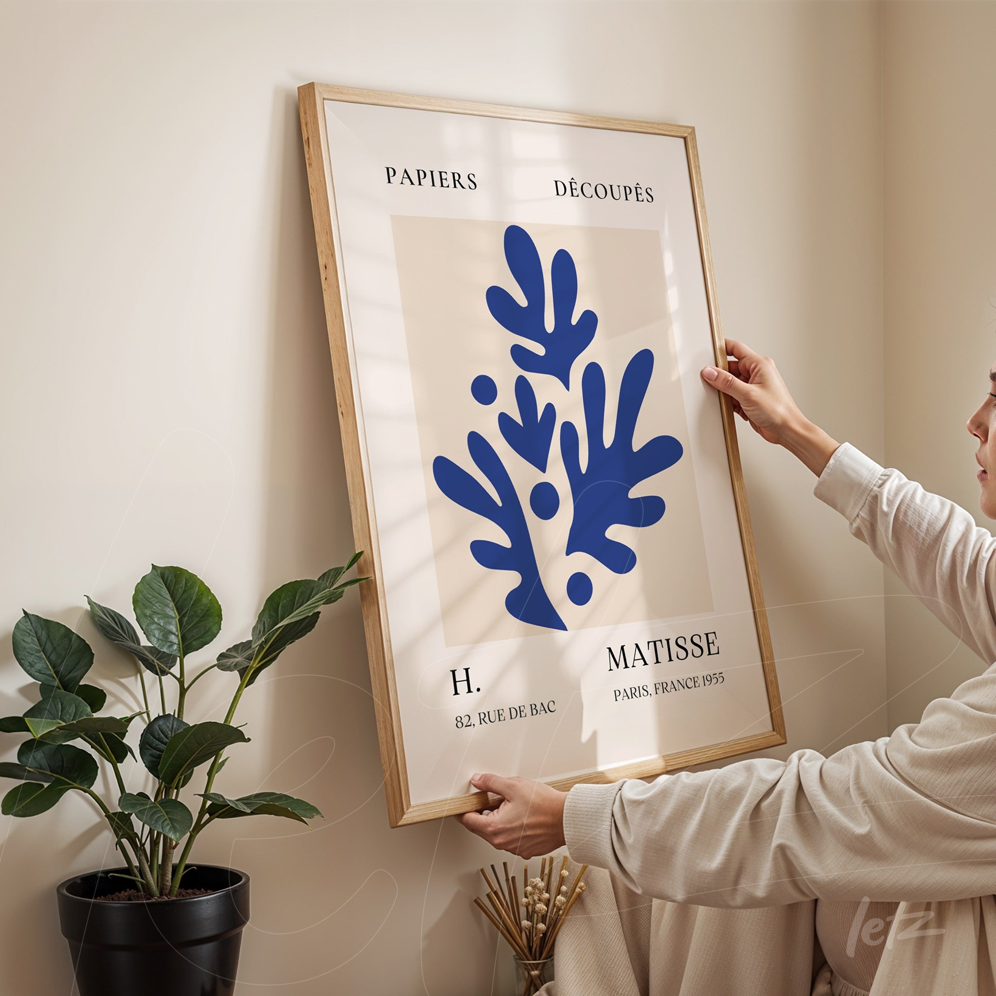 framed modern art featuring abstract blue shapes held by a person in front of a light-colored wall
