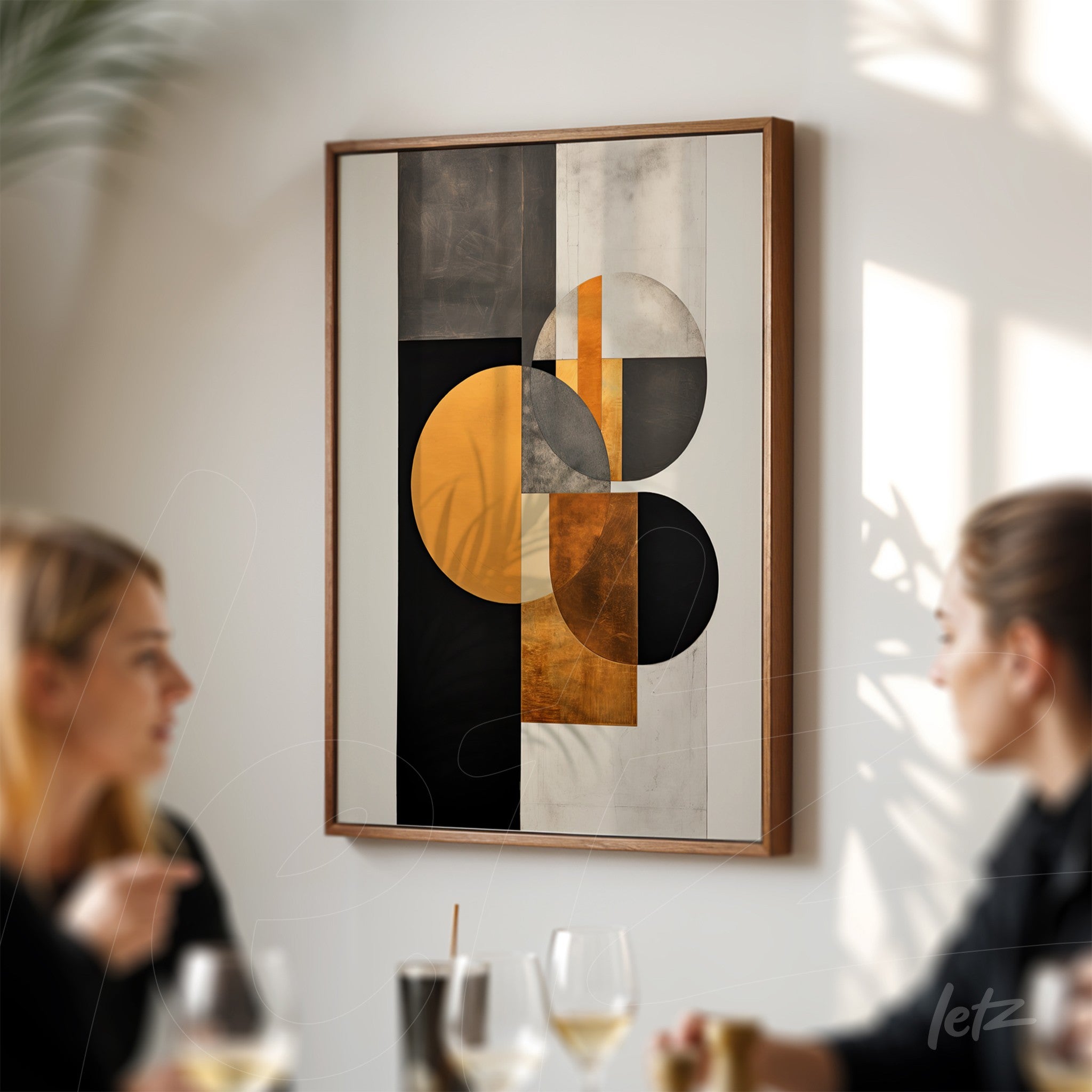 framed abstract wall art in black, orange, and gray displayed on a white wall with people in the background