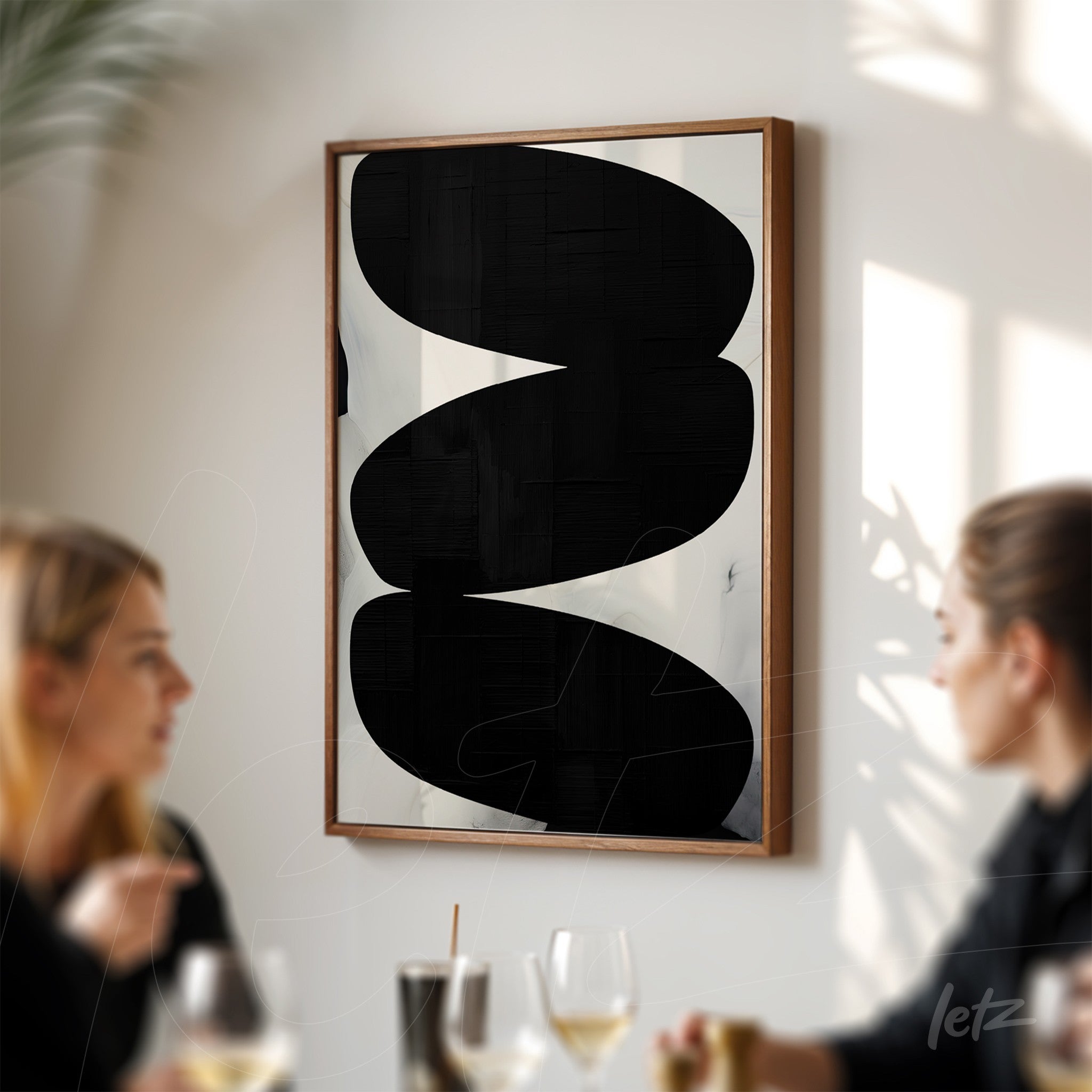 abstract wall art featuring black shapes on a light background in a light wood frame