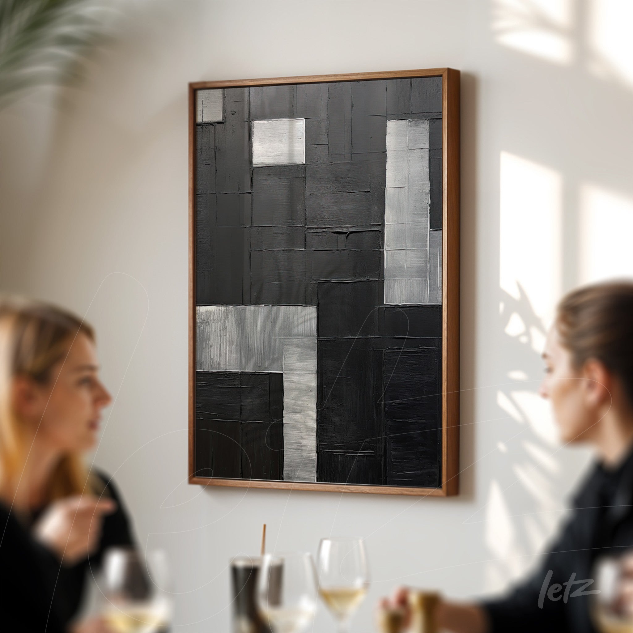 abstract wall art in black and silver tones in light wood frame displayed on a well-lit wall