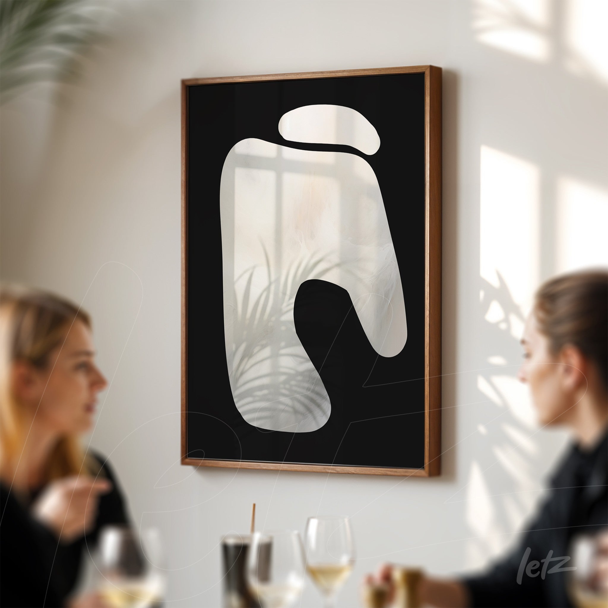 abstract wall art featuring organic shapes on a dark background with a light wood frame displayed in a softly lit setting