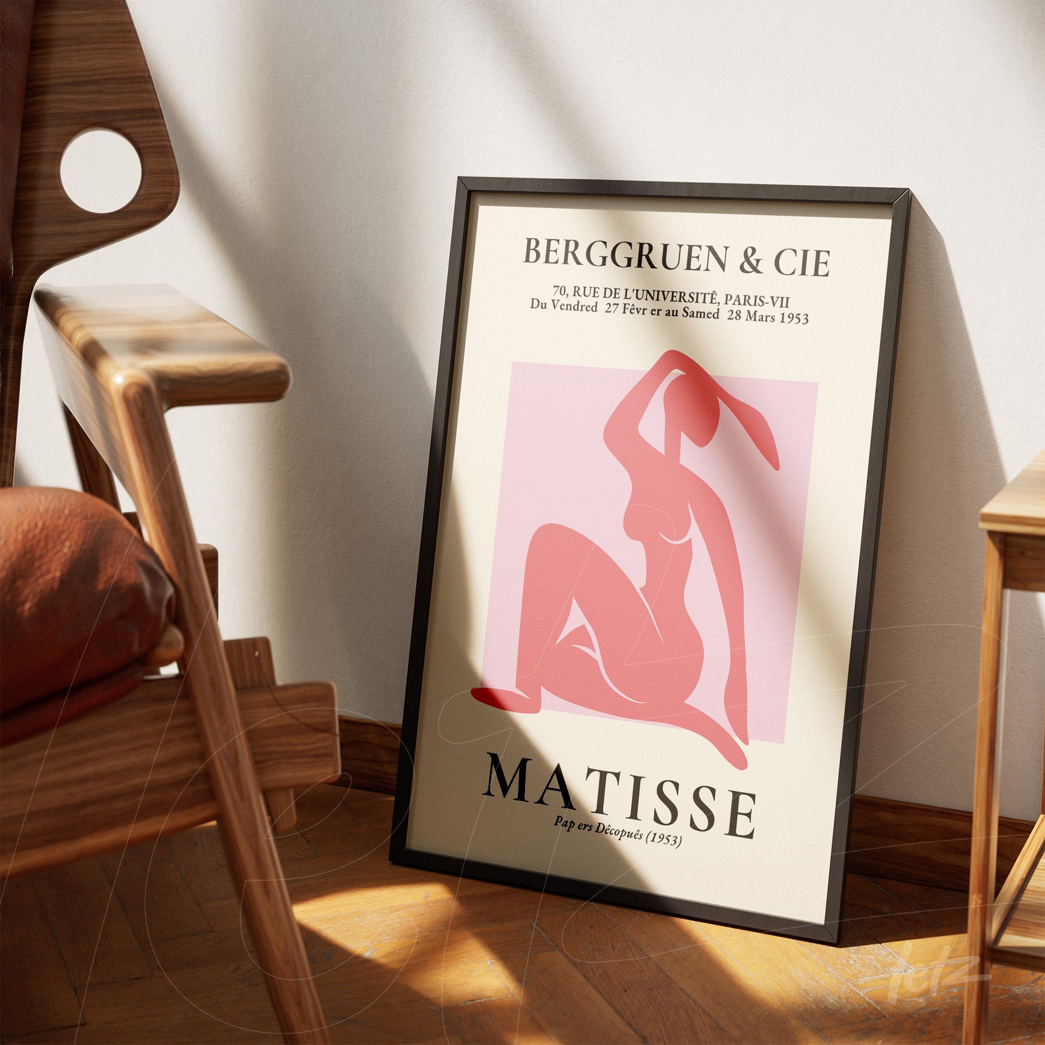 abstract wall art featuring a stylized female figure in shades of pink and red on a light background, framed in a thin black frame, leaning against a wooden chair