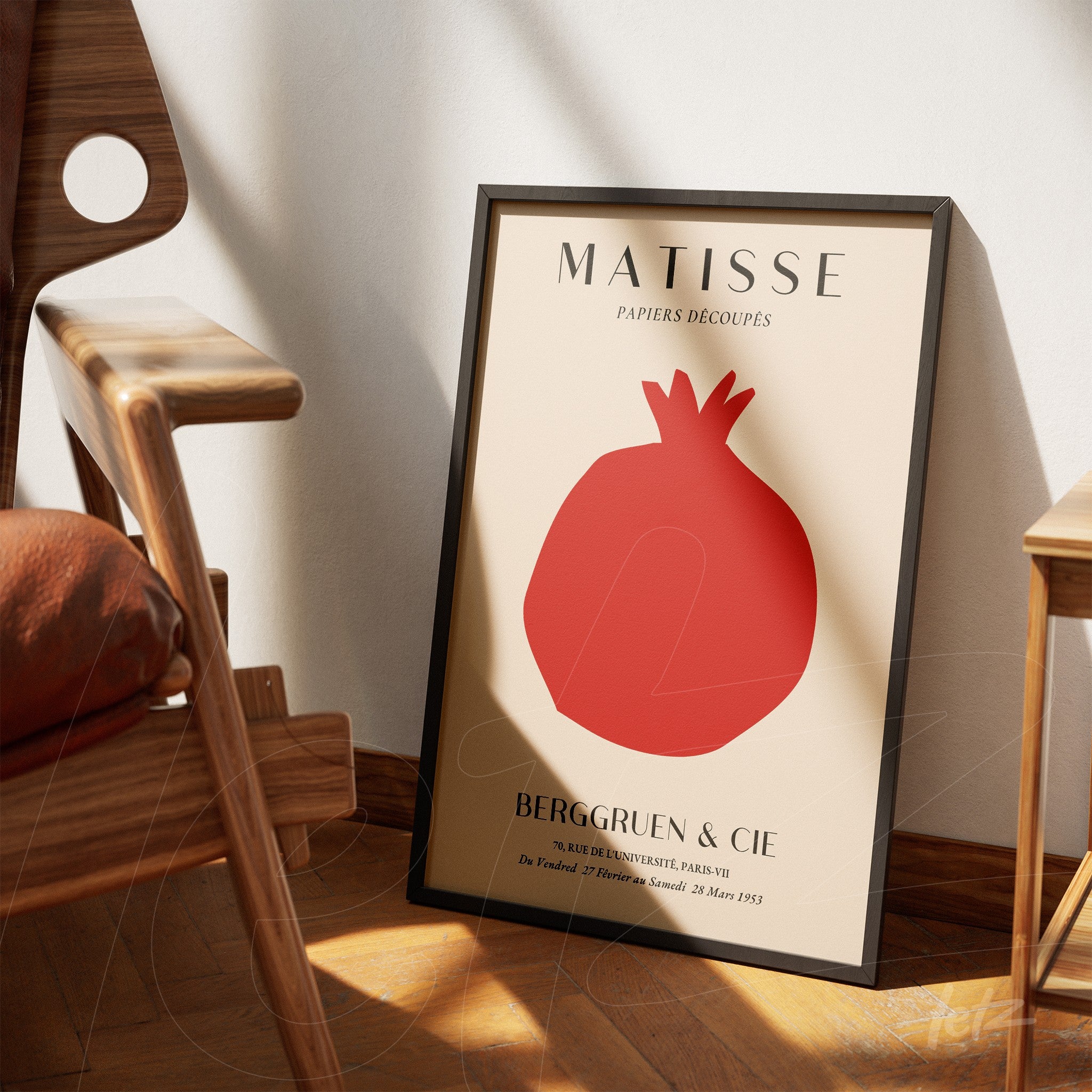 decorative art print inspired by Matisse featuring a red pomegranate silhouette on a light background framed in sleek black frame leaning beside a wooden chair