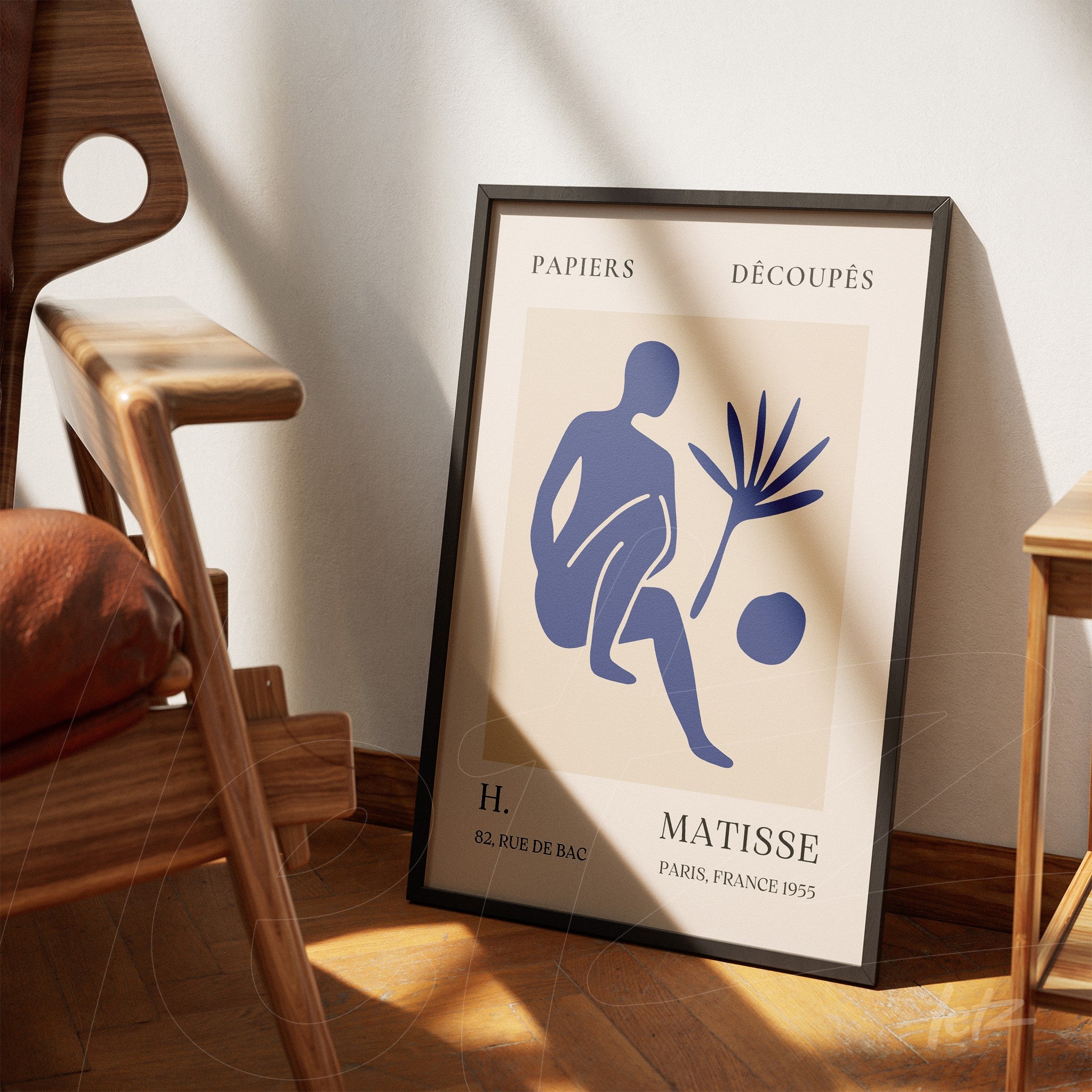 decorative wall art featuring modern design of human figure and plant in black frame leaning against light wall next to wooden chair