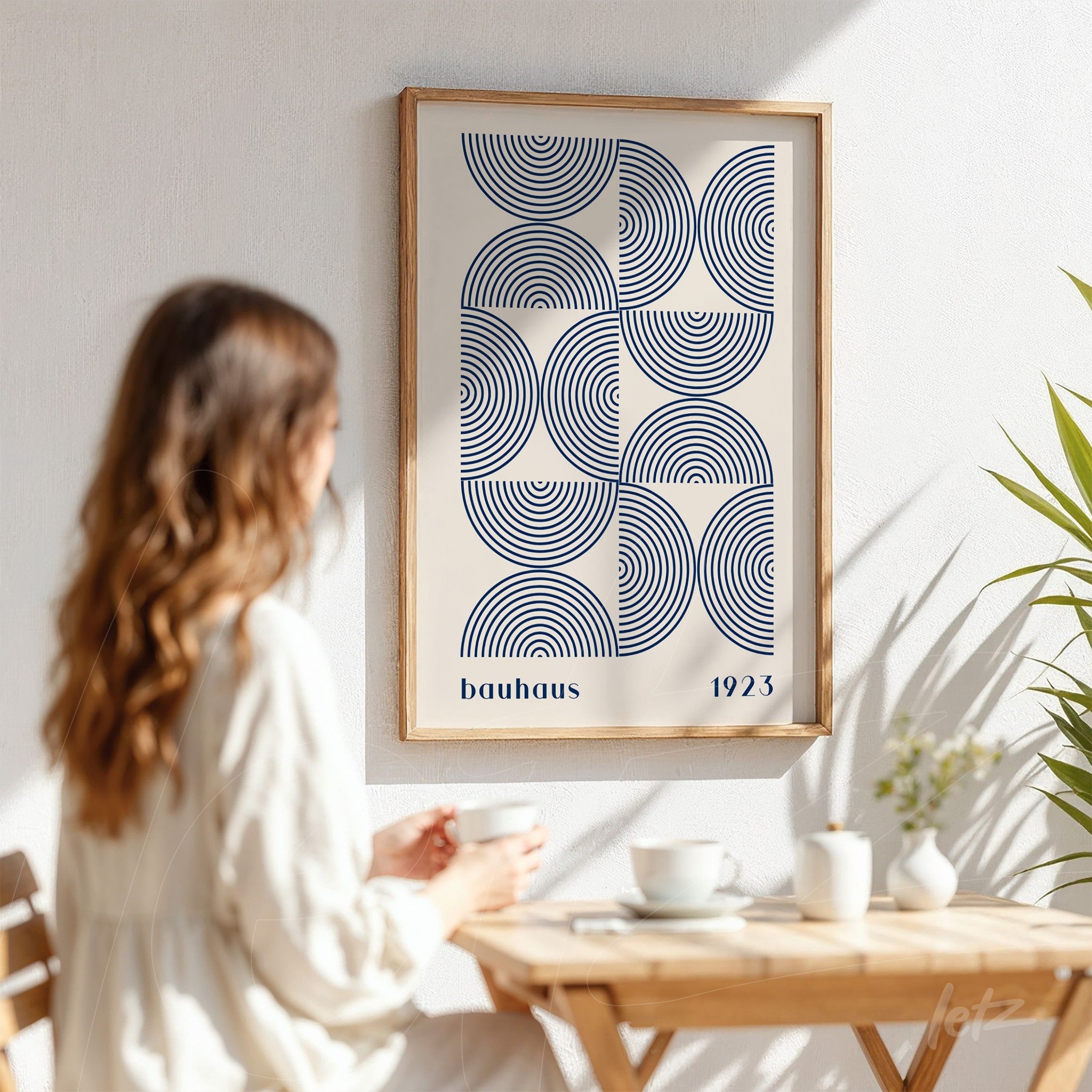 poster featuring geometric blue shapes in bauhaus style with light wood frame displayed on sunlit white wall