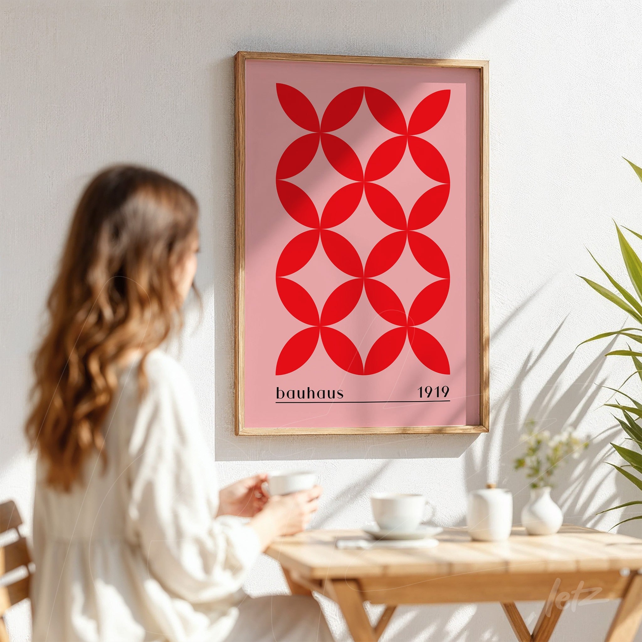 poster print featuring geometric Bauhaus style art with light wooden frame, displayed on a white wall next to a seated woman