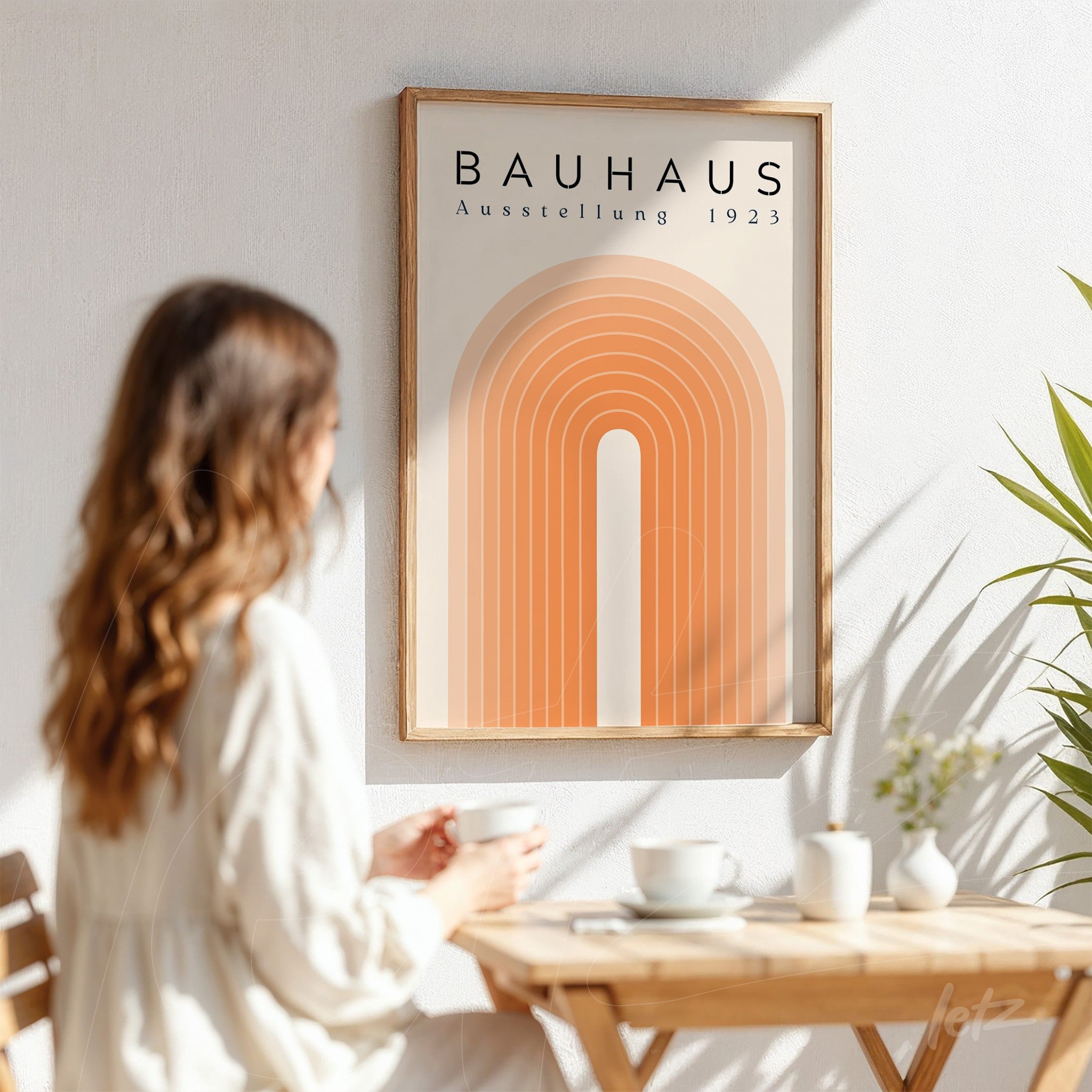 geometric bauhaus style wall art with orange arches in a light wood frame displayed on a white wall beside a person drinking coffee