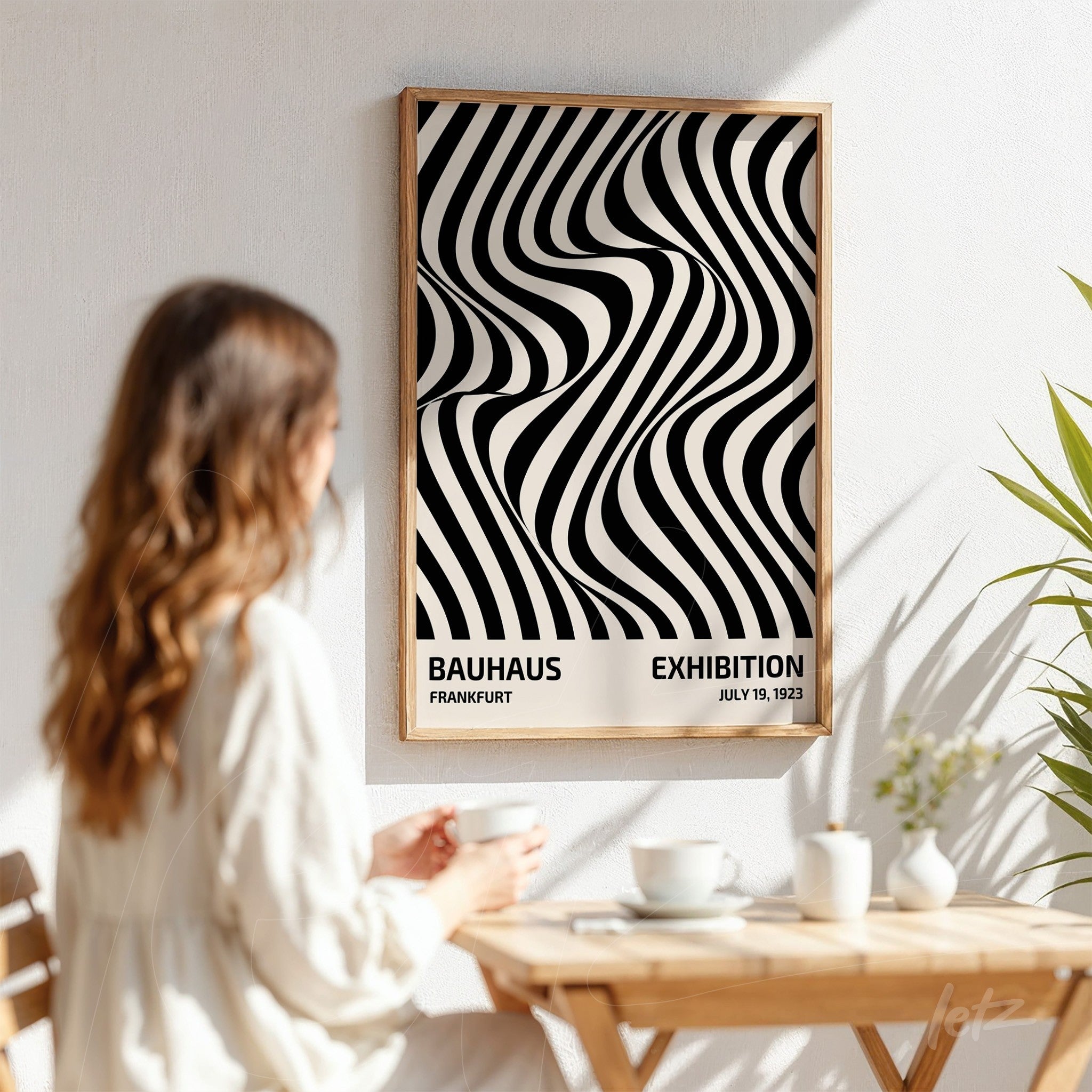 woman viewing abstract black and white poster with wavy pattern, light wood frame on white wall background