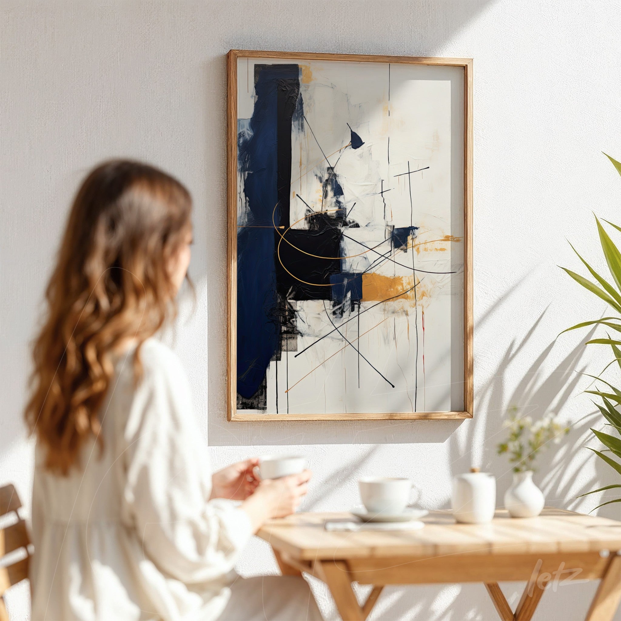 abstract painting featuring geometric shapes in shades of blue, yellow, and black, in a light wood frame displayed on a white wall with a nearby plant