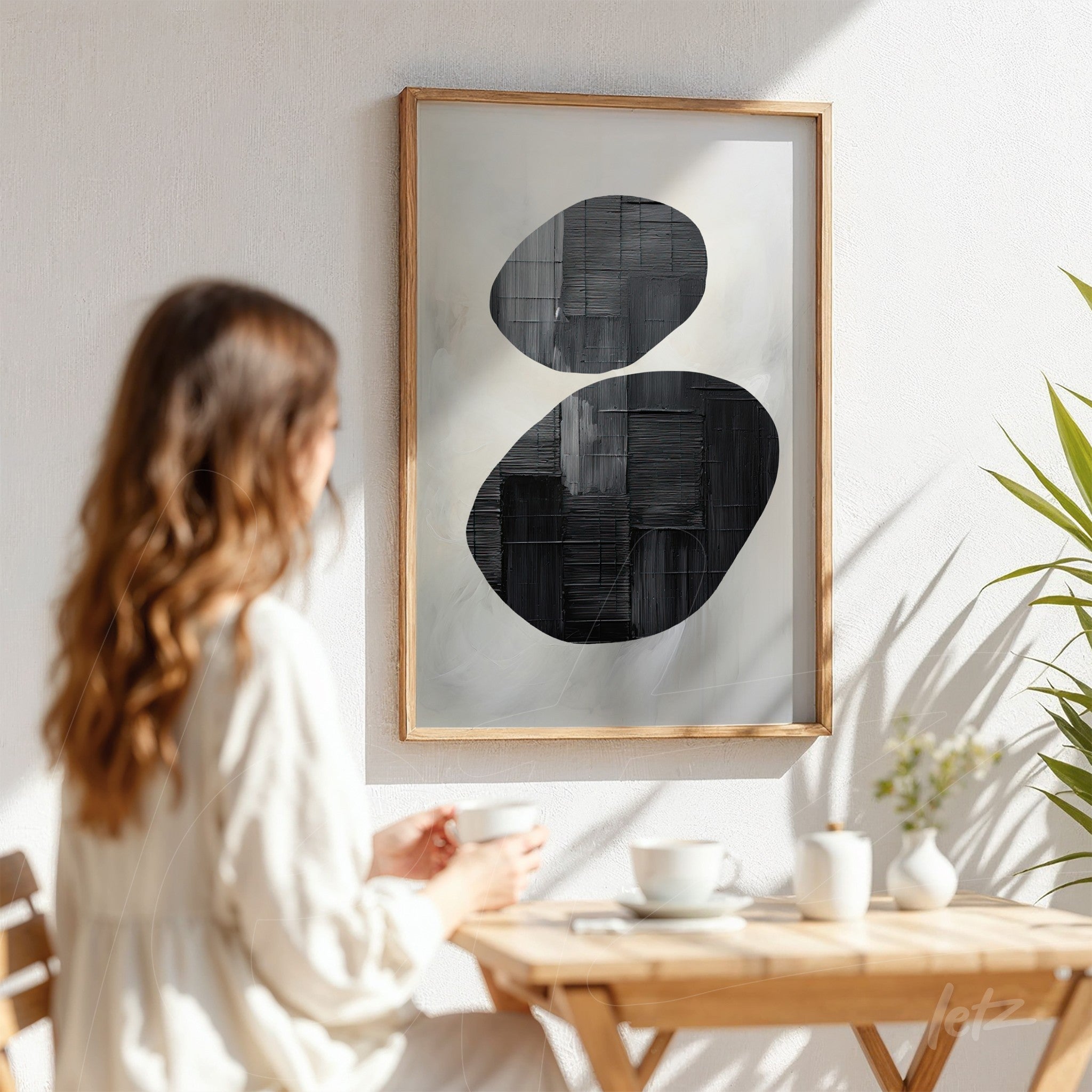 abstract wall art in light wood frame featuring black shapes on light background displayed in a bright setting