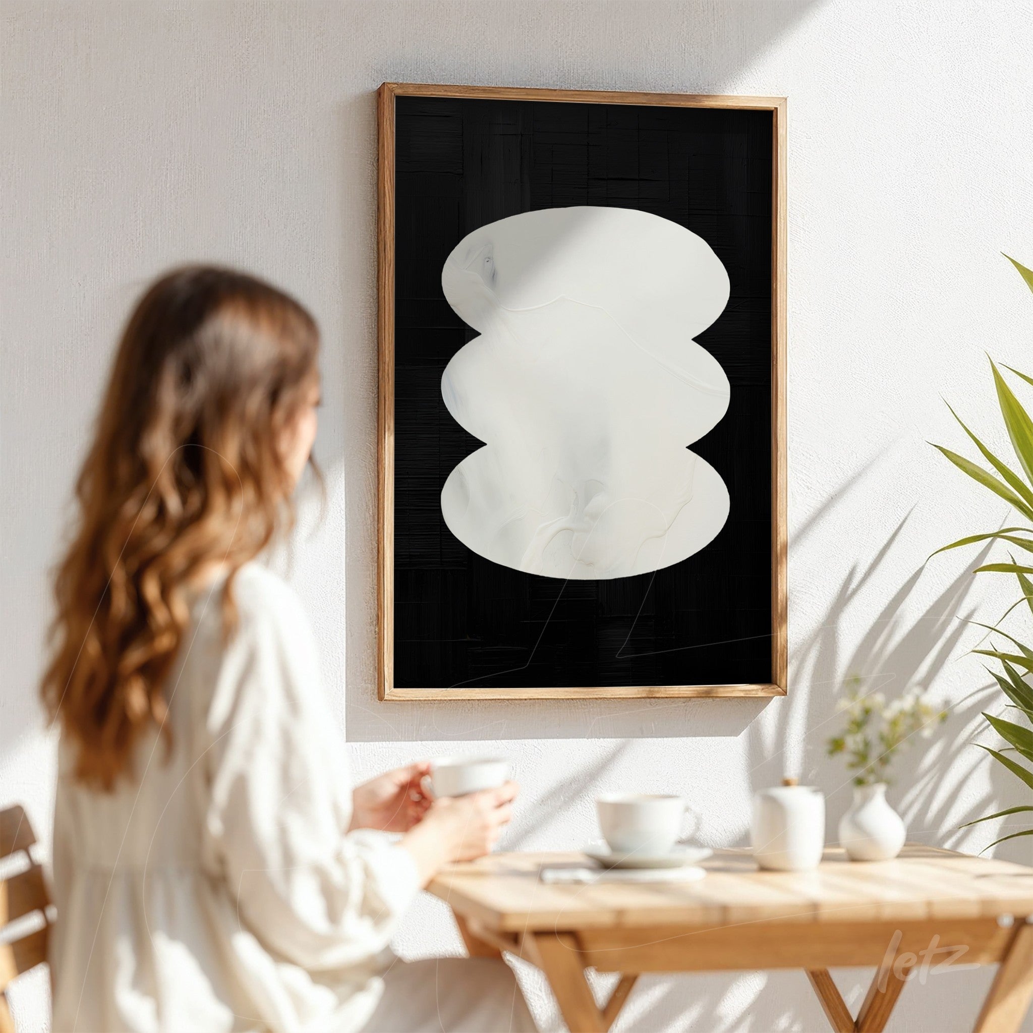 modern abstract wall art featuring white shapes on black background in a light wood frame displayed against a white wall with a plant nearby