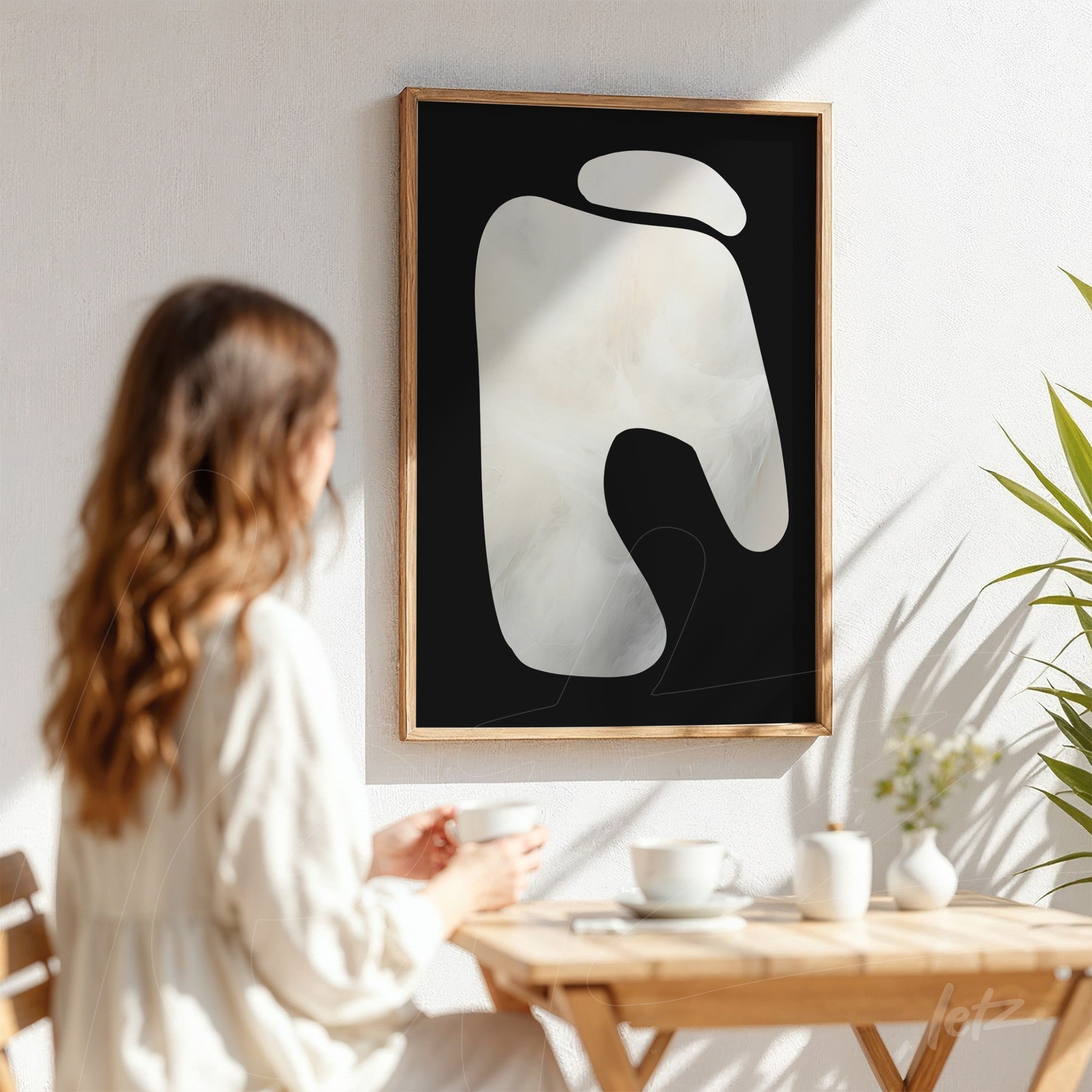 abstract wall art featuring organic shapes on a black background, framed in light wood, displayed in a naturally lit setting