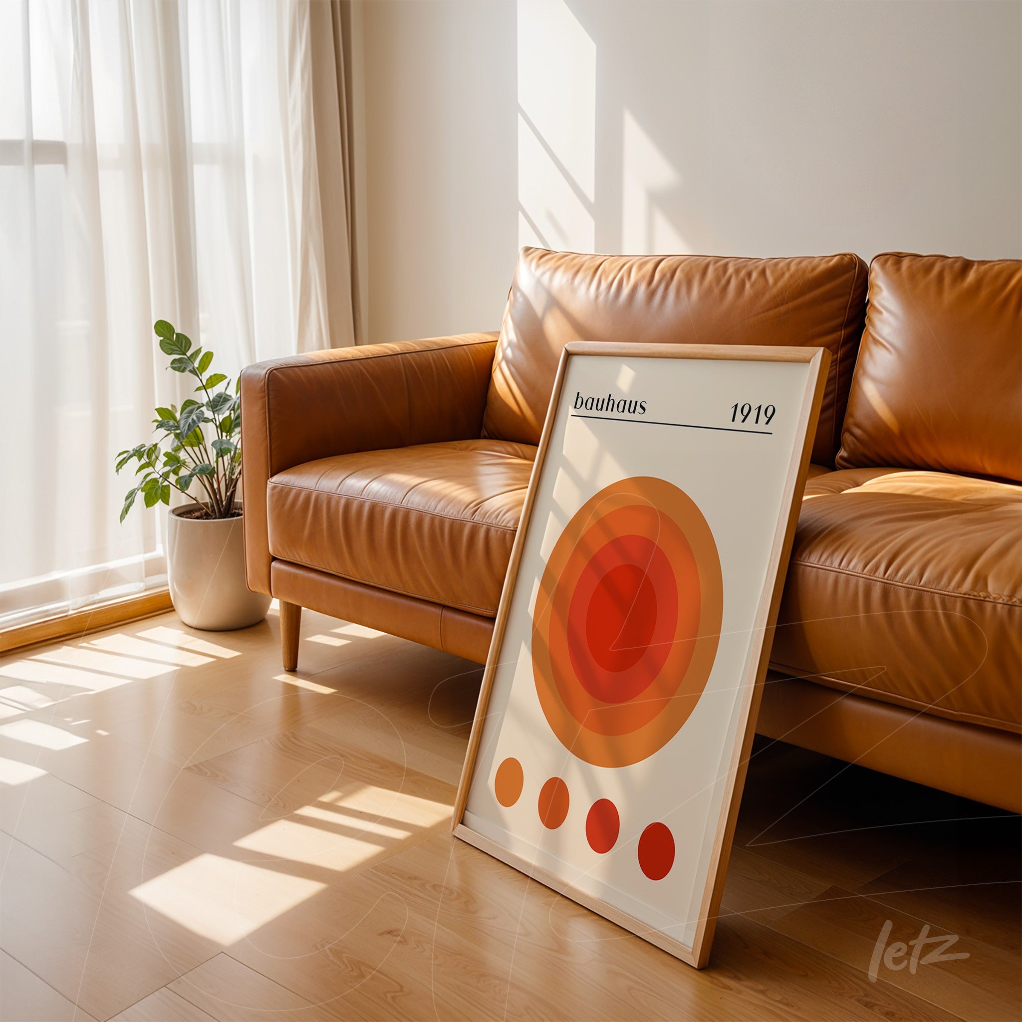 framed bauhaus style geometric art featuring concentric circles in shades of orange, leaning against a brown leather sofa in a well-lit room