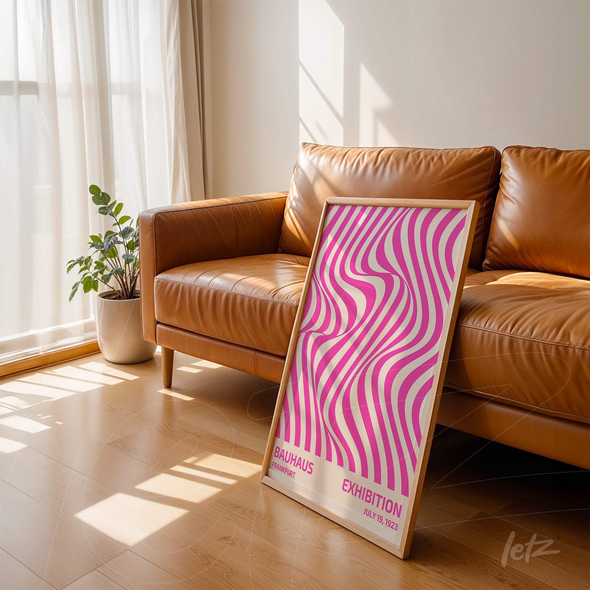 framed art with pink and white geometric design, light wood frame, leaning against a leather sofa in a well-lit living room
