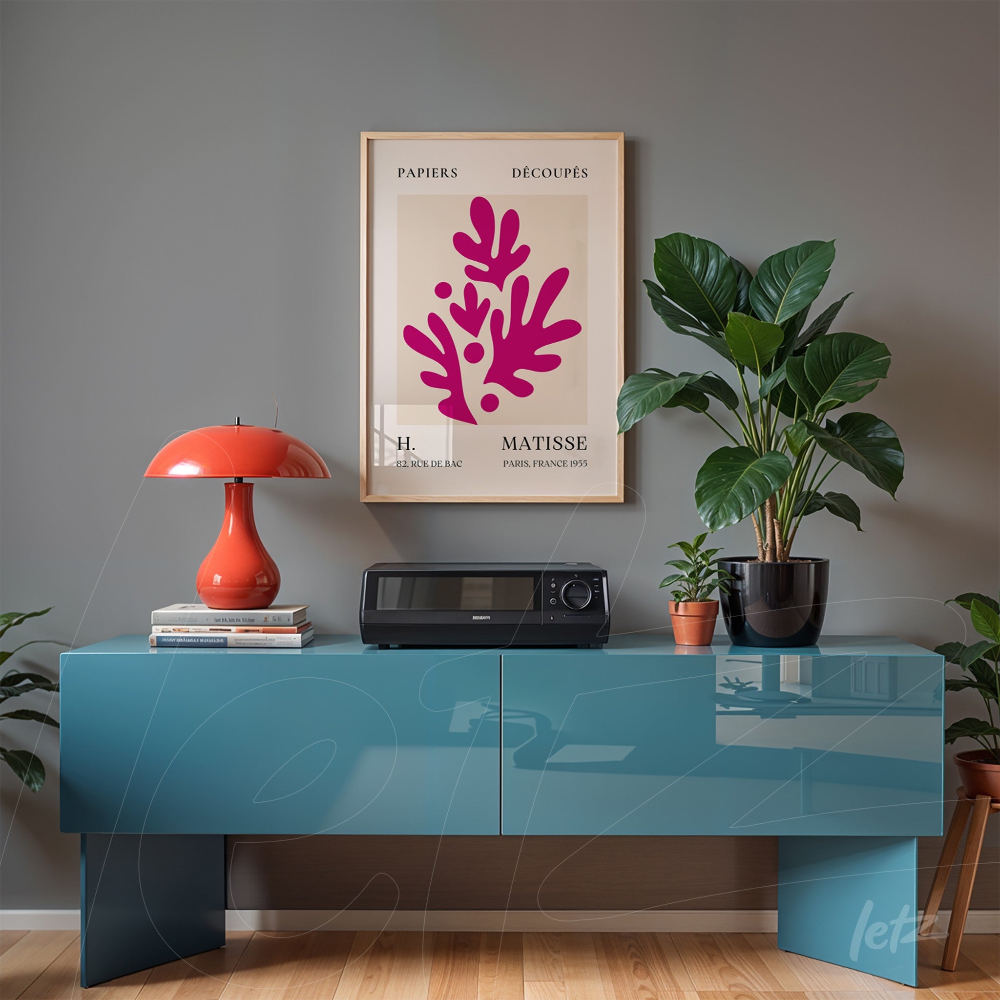 framed modern artwork featuring coral shapes in pink on gray wall beside a red lamp and black potted plant