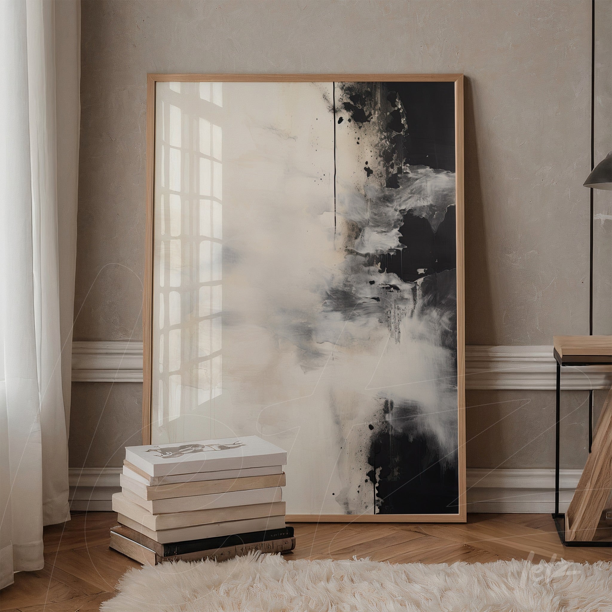 abstract art piece in light and dark tones in a light wood frame leaning against a table next to stacked books
