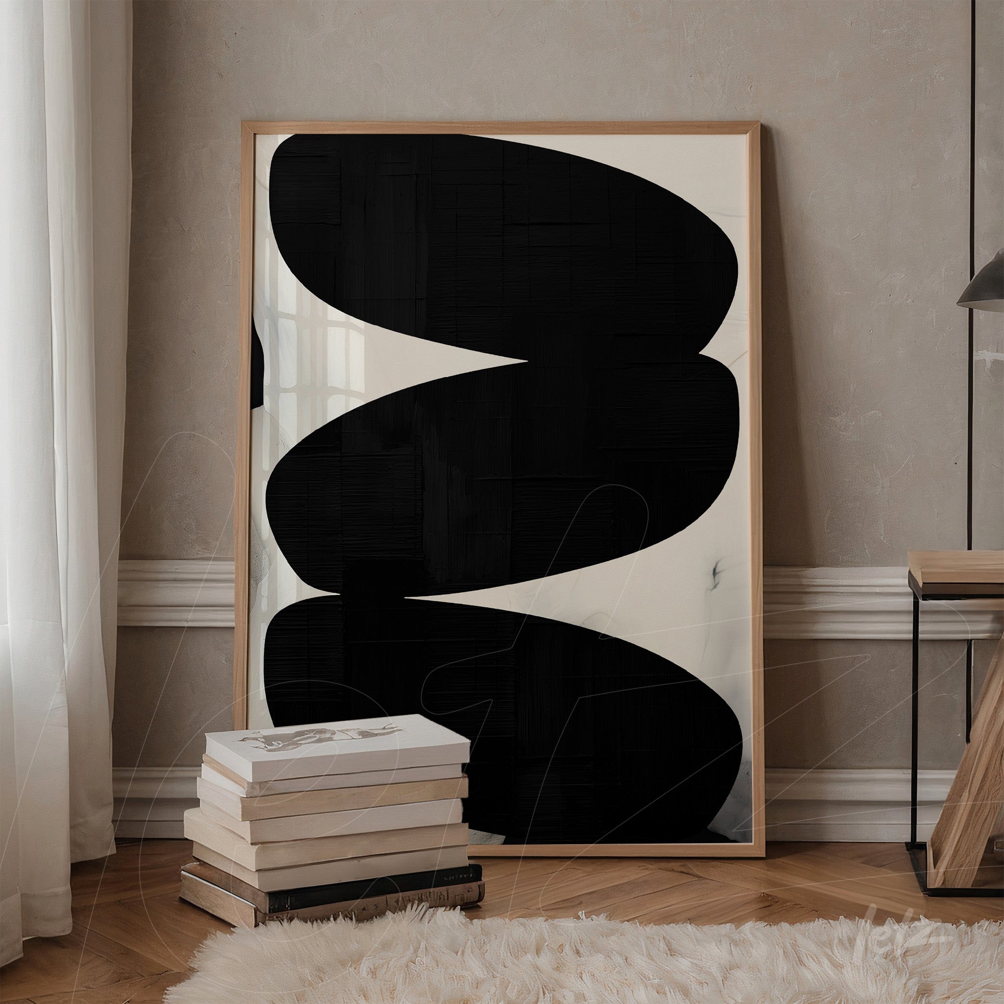 framed wall art featuring black and white abstract shapes leaning against a stack of books on a side table next to a textured light wall