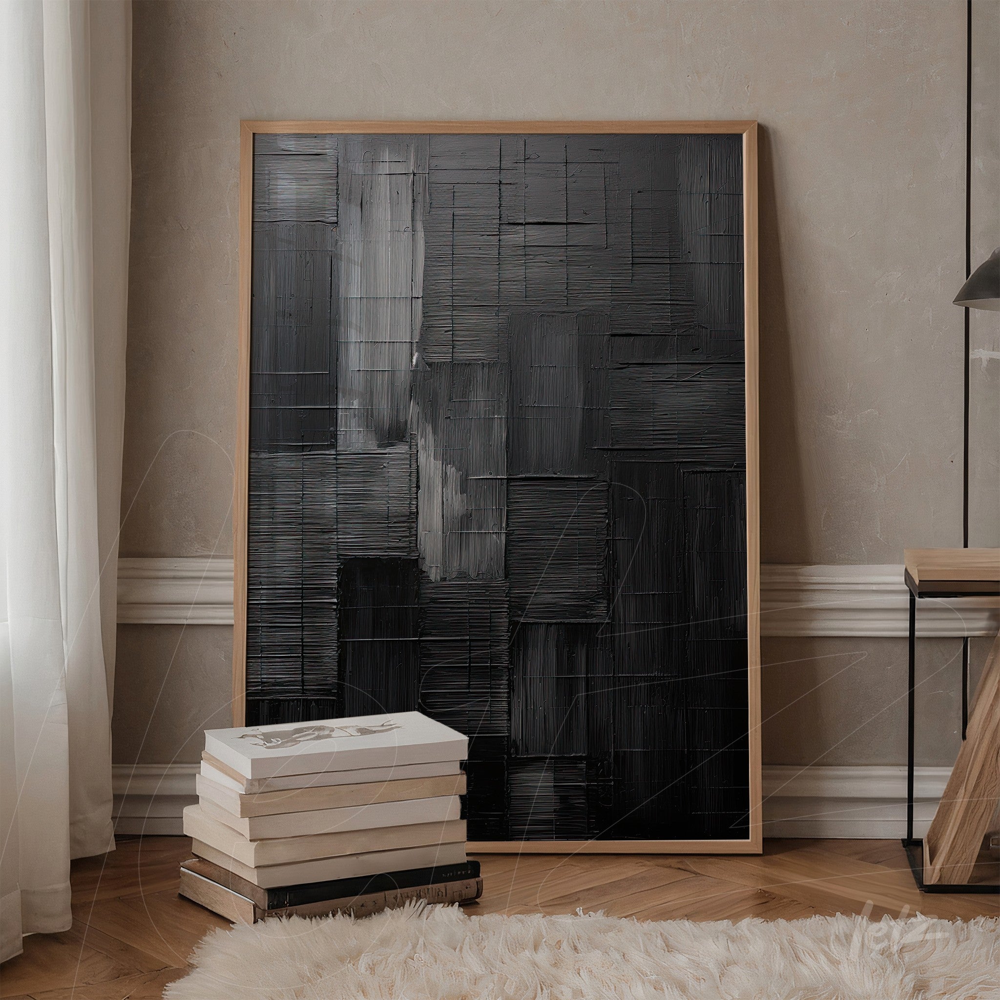 abstract wall art featuring textured black tones, framed in light wood and leaning against a stack of books in an elegant setting