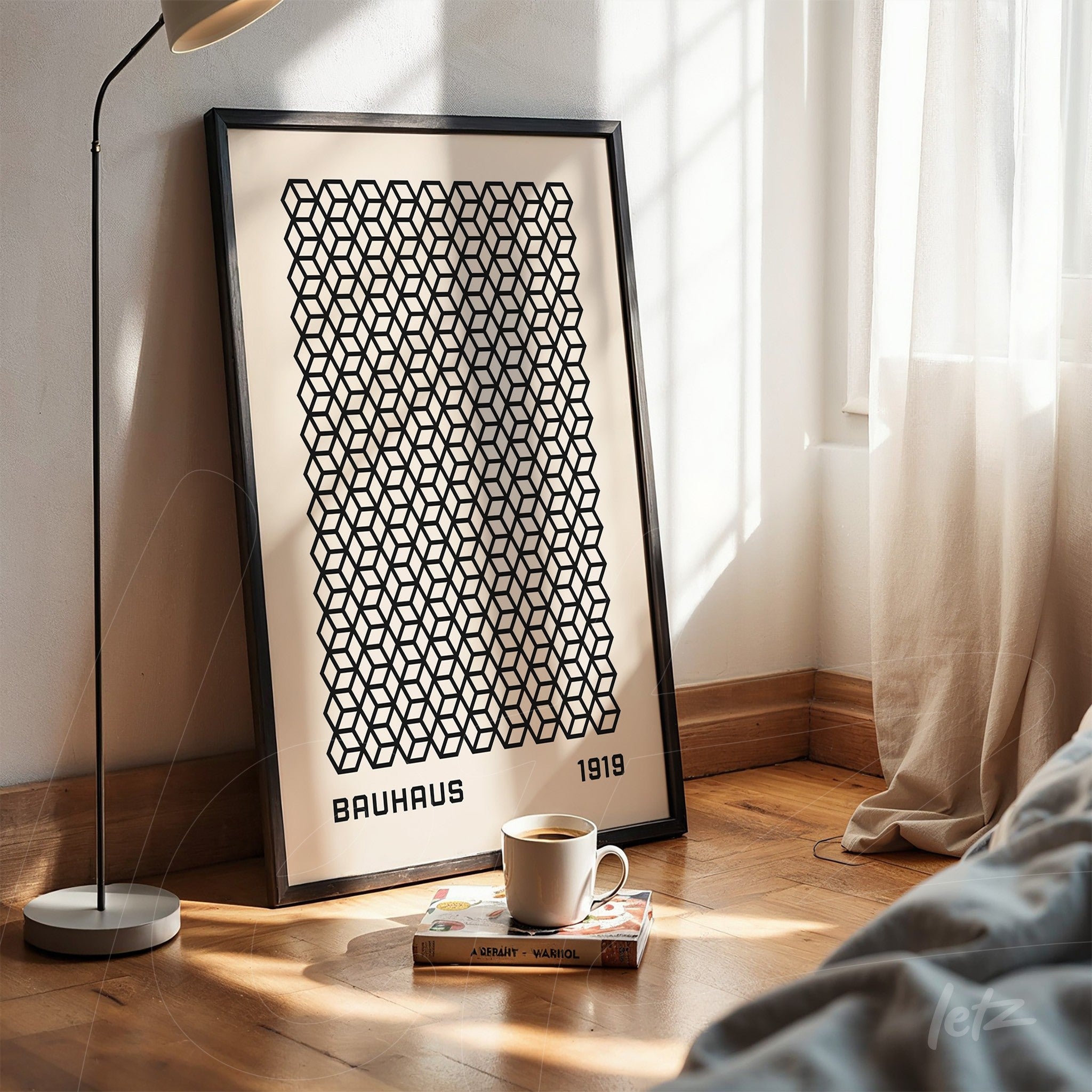 poster with black geometric pattern and text bauhaus 1919 in a thin black frame, resting on wooden floor next to a modern lamp and a window with sheer curtain