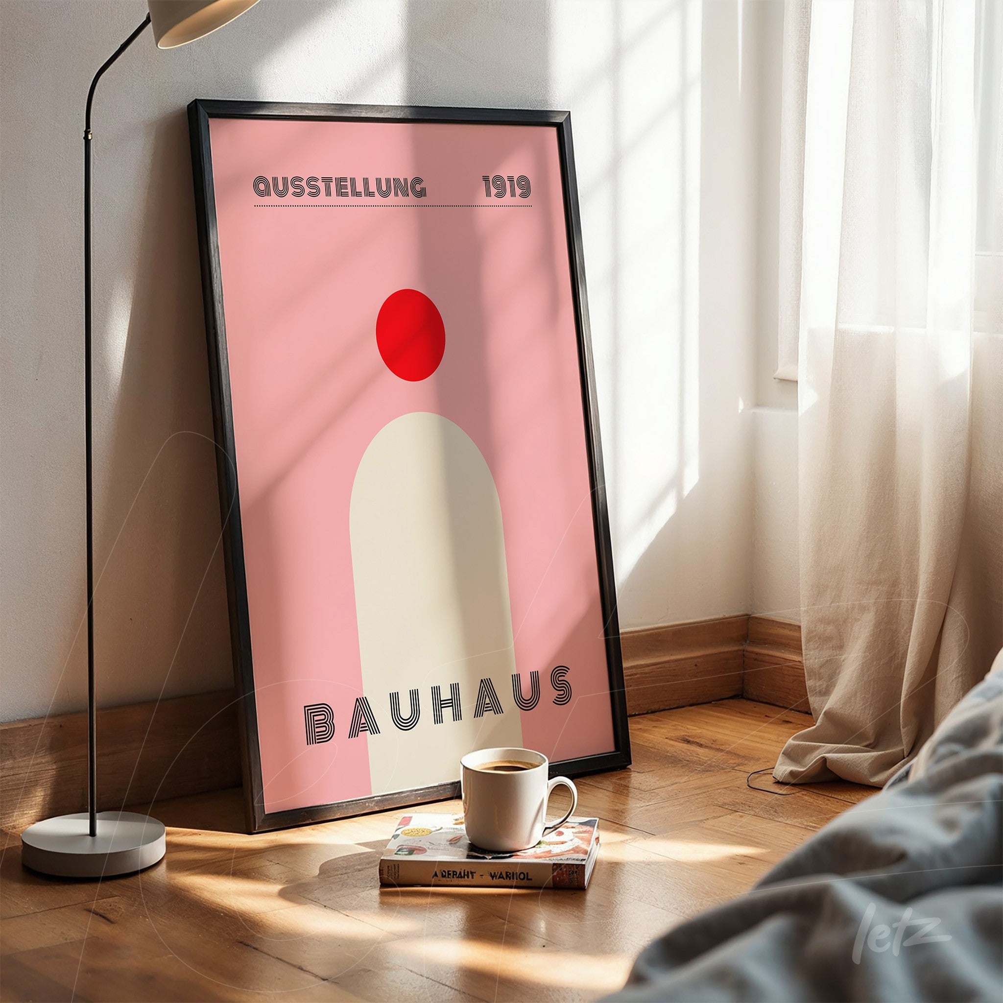 minimalistic poster print of Bauhaus movement art displayed in black frame on wooden floor next to coffee cup