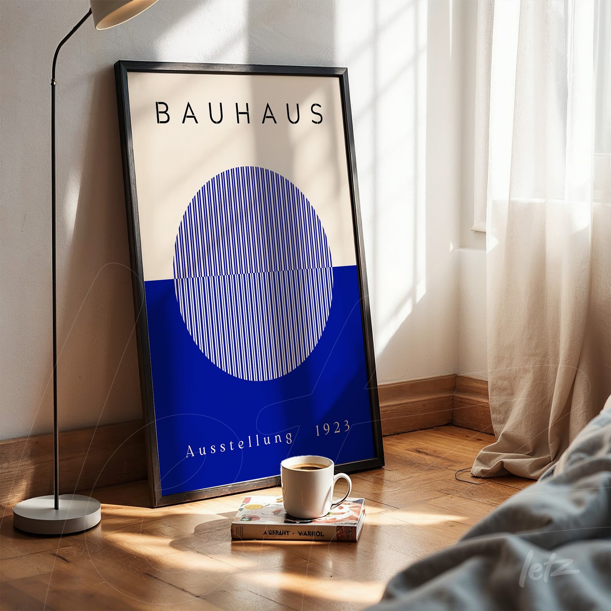 bauhaus poster print with blue sphere and white lines in black frame, resting on wooden floor next to coffee cup