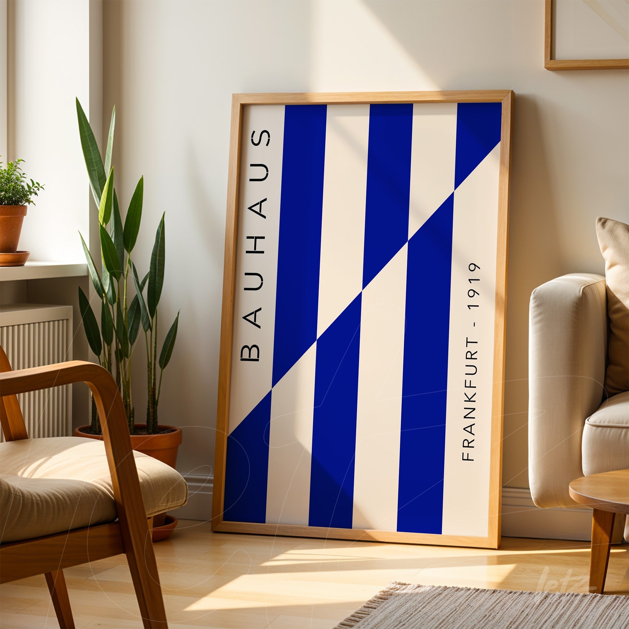 poster print with geometric blue and white design labeled 'bauhaus frankfurt 1919' in light wood frame leaning against a sunlit living room wall