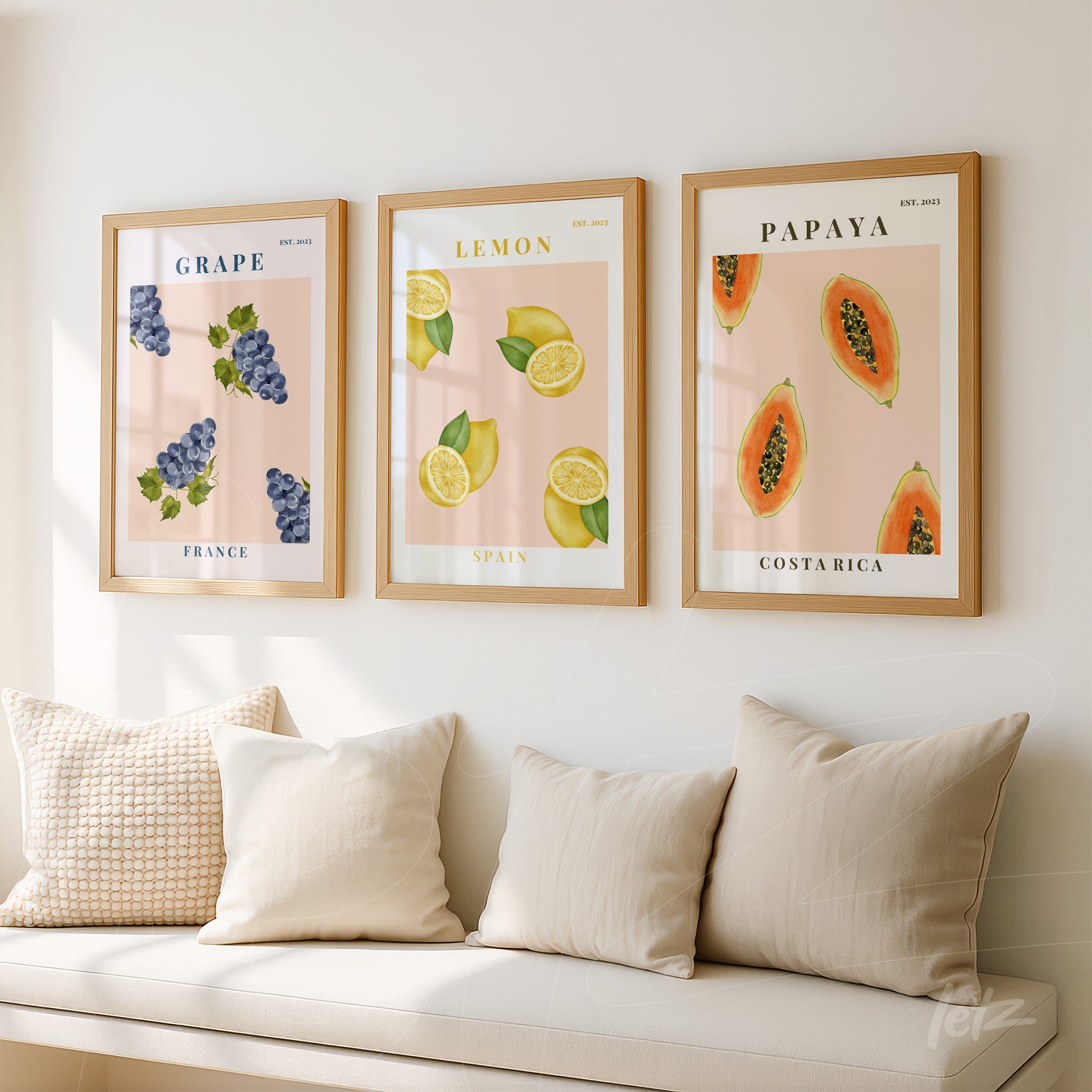 set of framed illustrations featuring grapes, lemons, and papaya in light wooden frames displayed on a white wall with light-colored sofas in the background